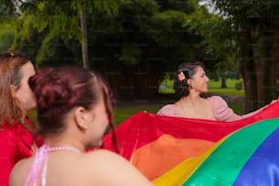 un groupe de femmes debout les unes autour des autres tenant un drapeau arc-en-ciel