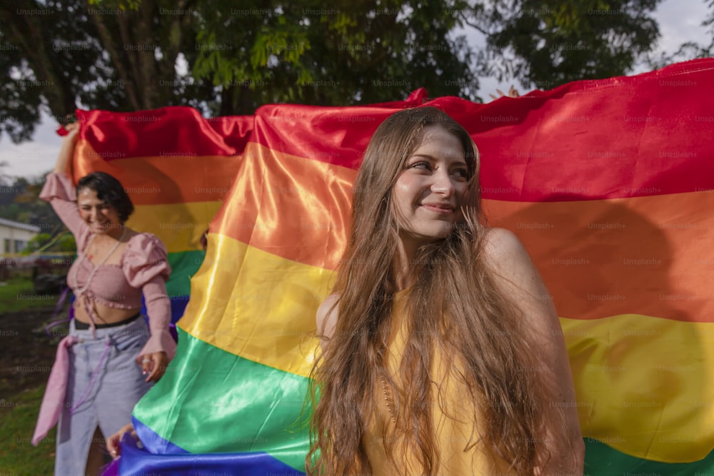 a woman standing next to a rainbow colored flag