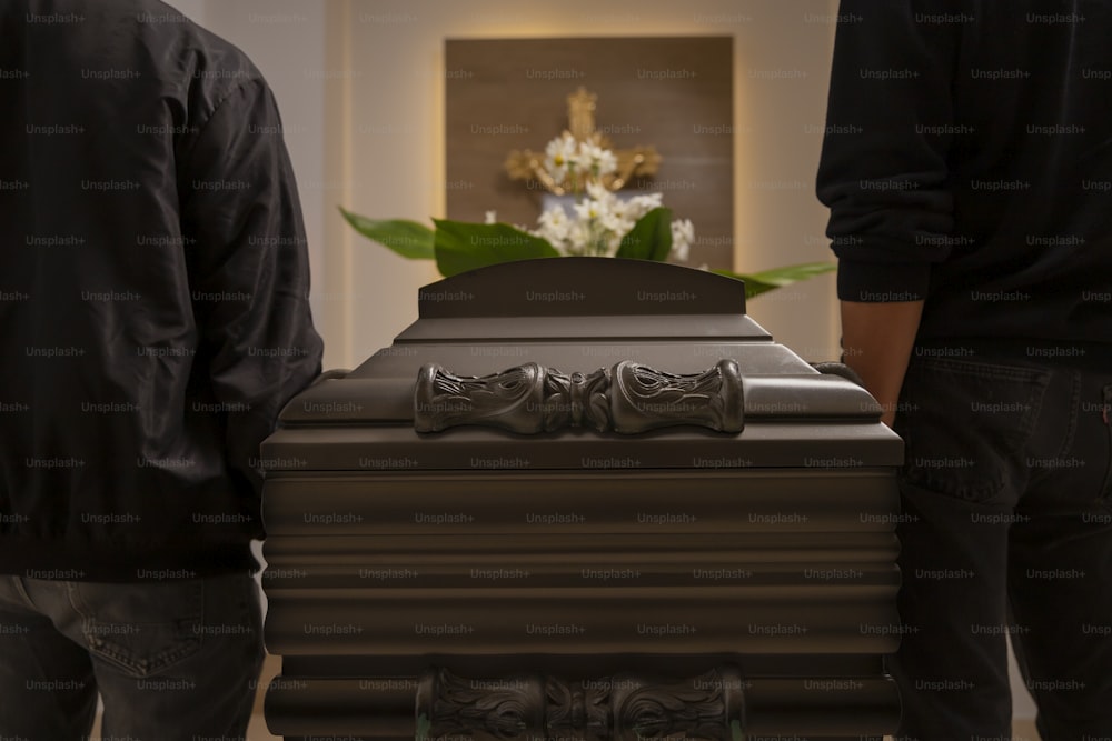 a couple of men standing next to a brown casket