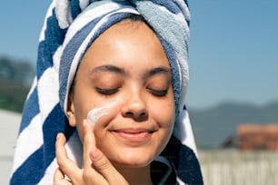 a woman with a towel on her head is applying a cream on her face