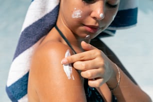 a woman with a towel on her head is applying cream on her arm