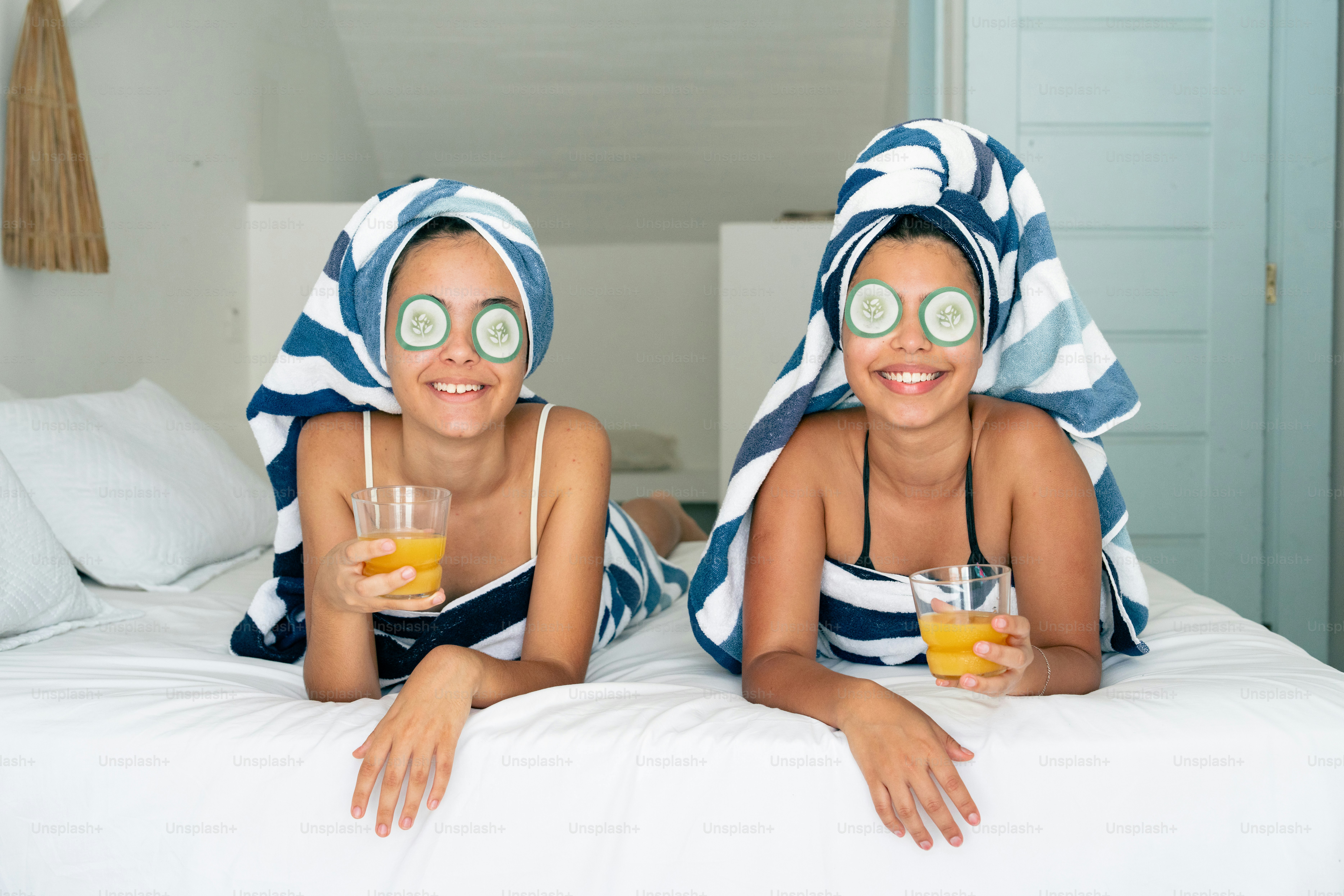two girls wearing cucumber towels and cucumbers on a bed