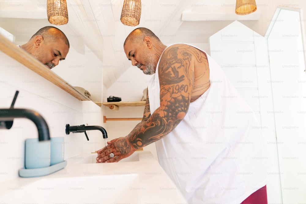 a man with a tattooed arm standing in front of a bathroom sink