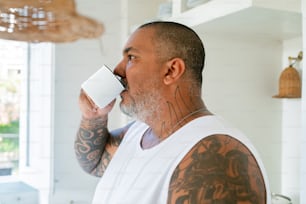 un uomo con tatuaggi che beve da una tazza