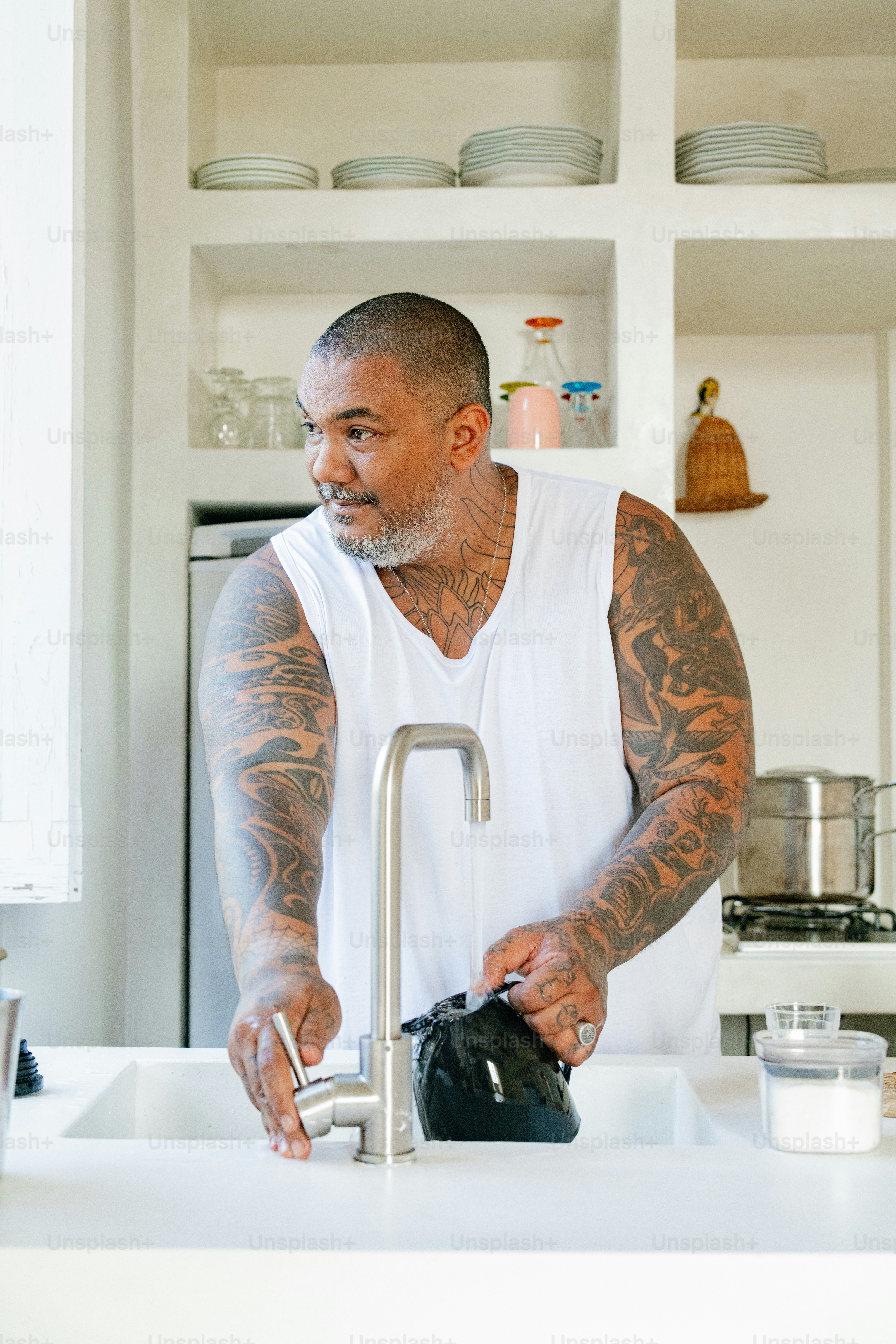 a tattooed man washing his hands in a kitchen sink