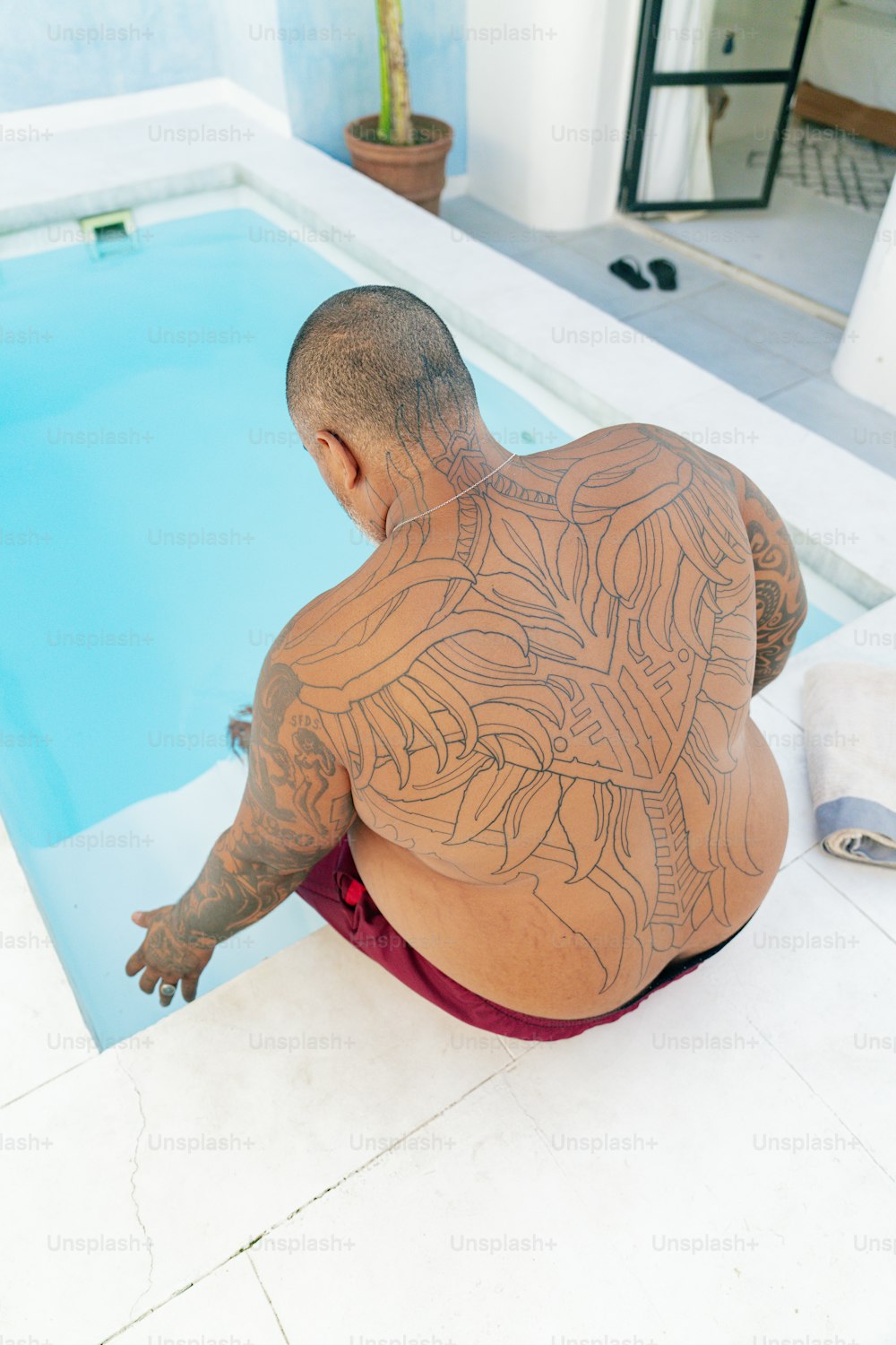 a man with a tattoo on his back sitting in front of a swimming pool