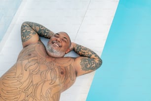 a man with tattoos on his body laying next to a swimming pool