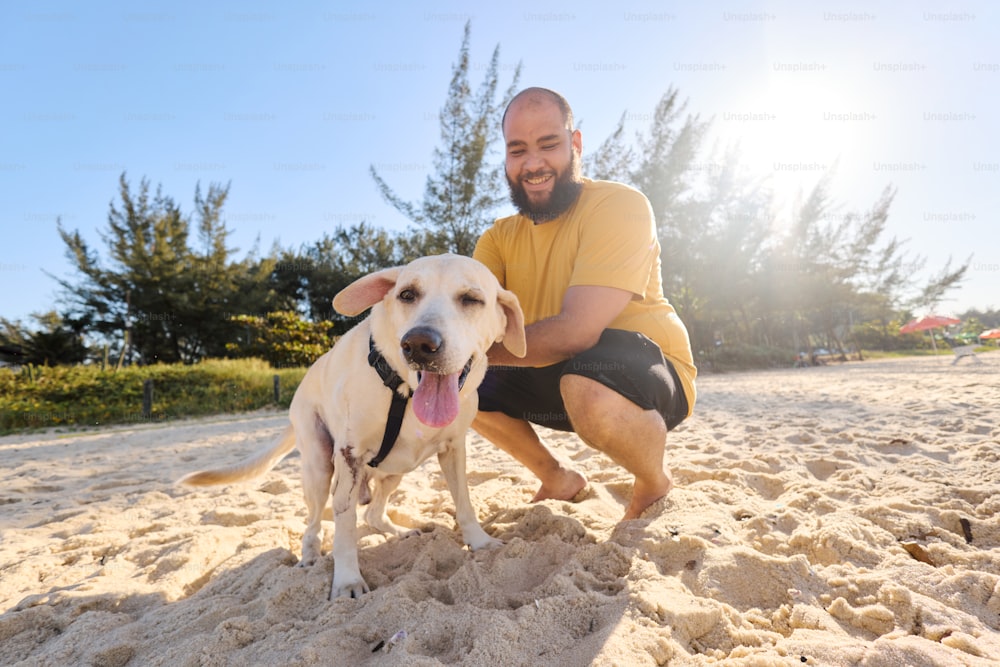 a man kneeling down next to a dog on a sandy beach