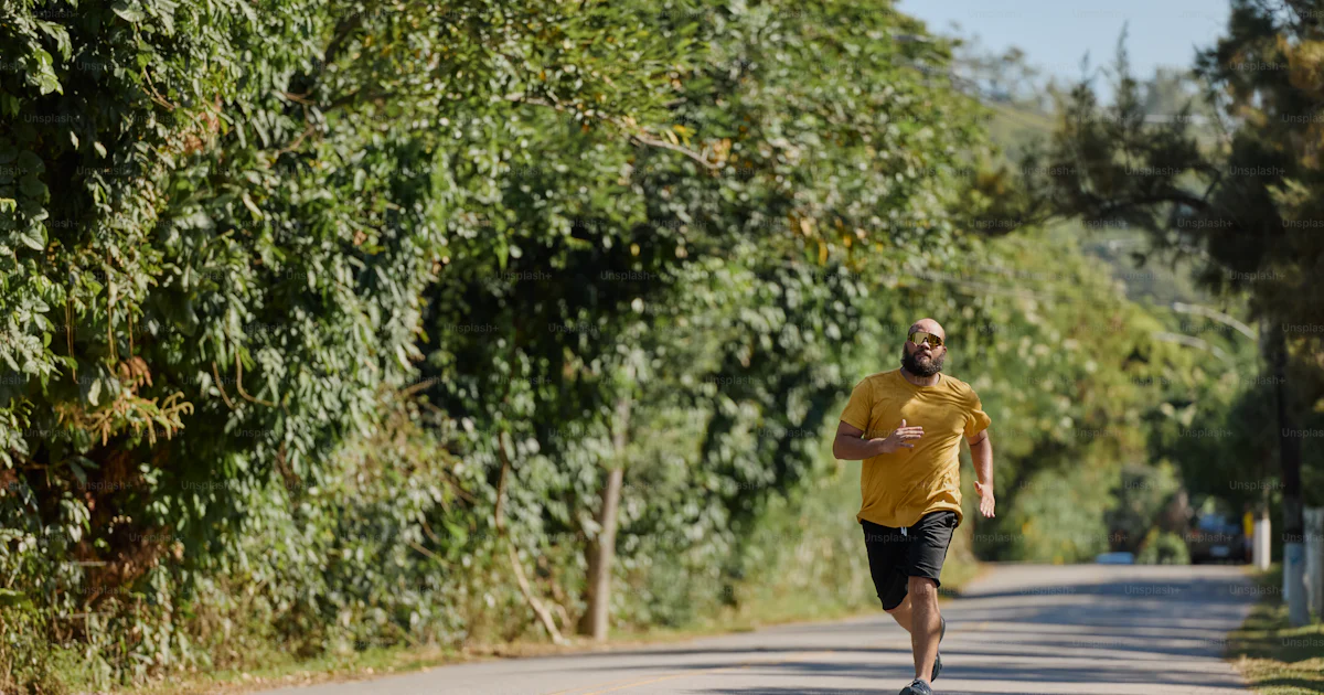 Un Running A man in a yellow shirt running down a road photo – Excercising Image ...