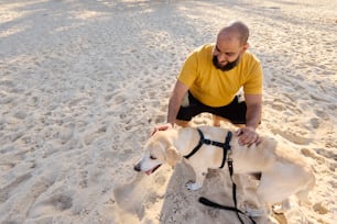 un uomo inginocchiato accanto a due cani su una spiaggia