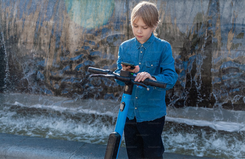 a young boy holding a blue scooter in front of a fountain