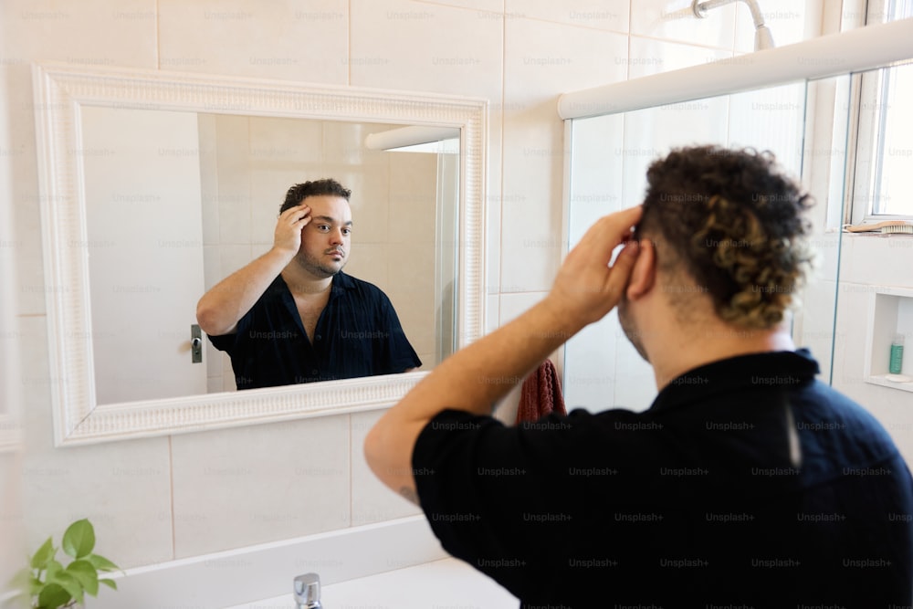 a man standing in front of a bathroom mirror brushing his hair