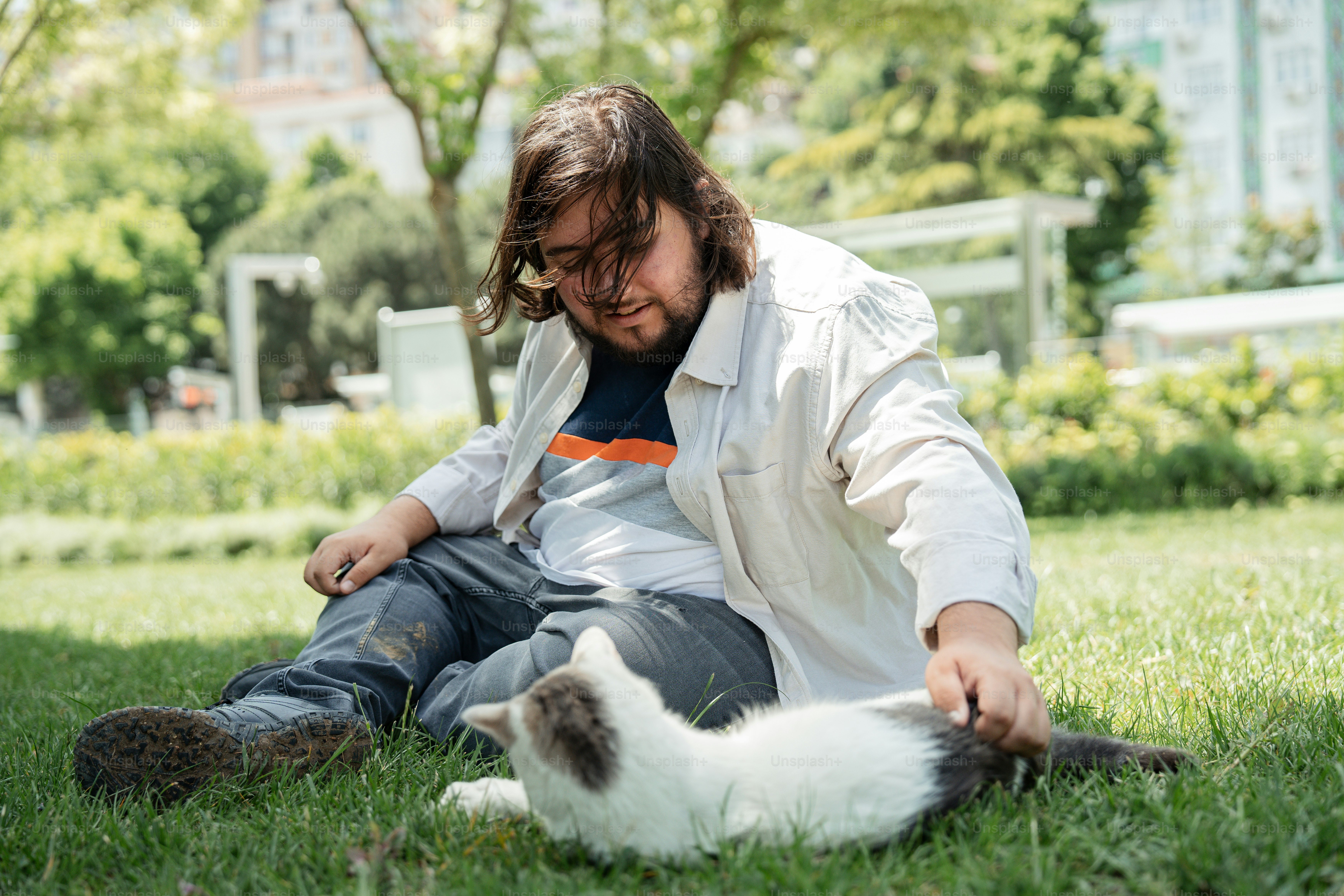 草むらに座って猫を撫でる男