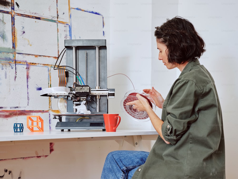 Una donna seduta a un tavolo che lavora su una stampante 3D