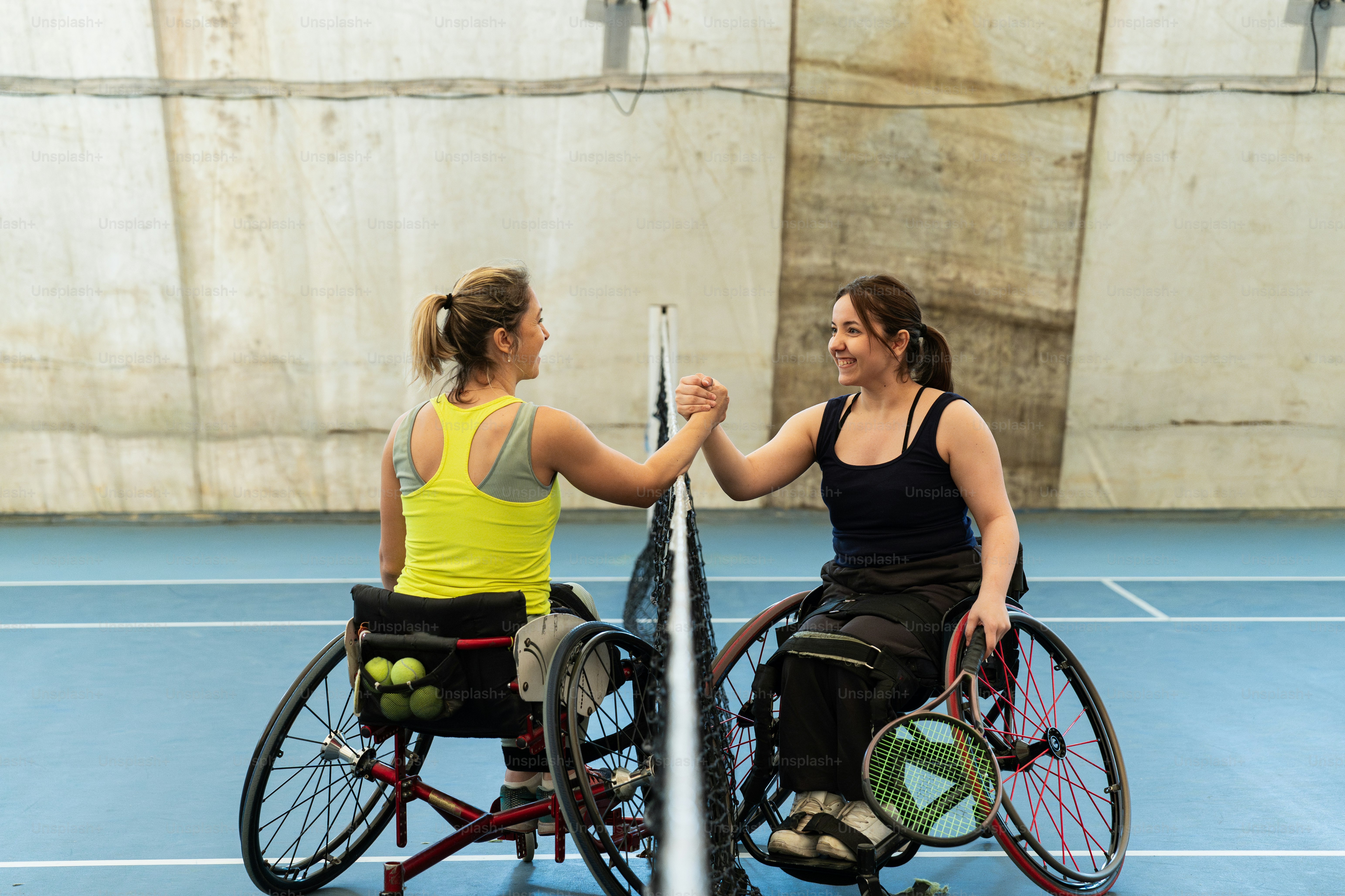 two women in wheelchairs shaking hands on a tennis court