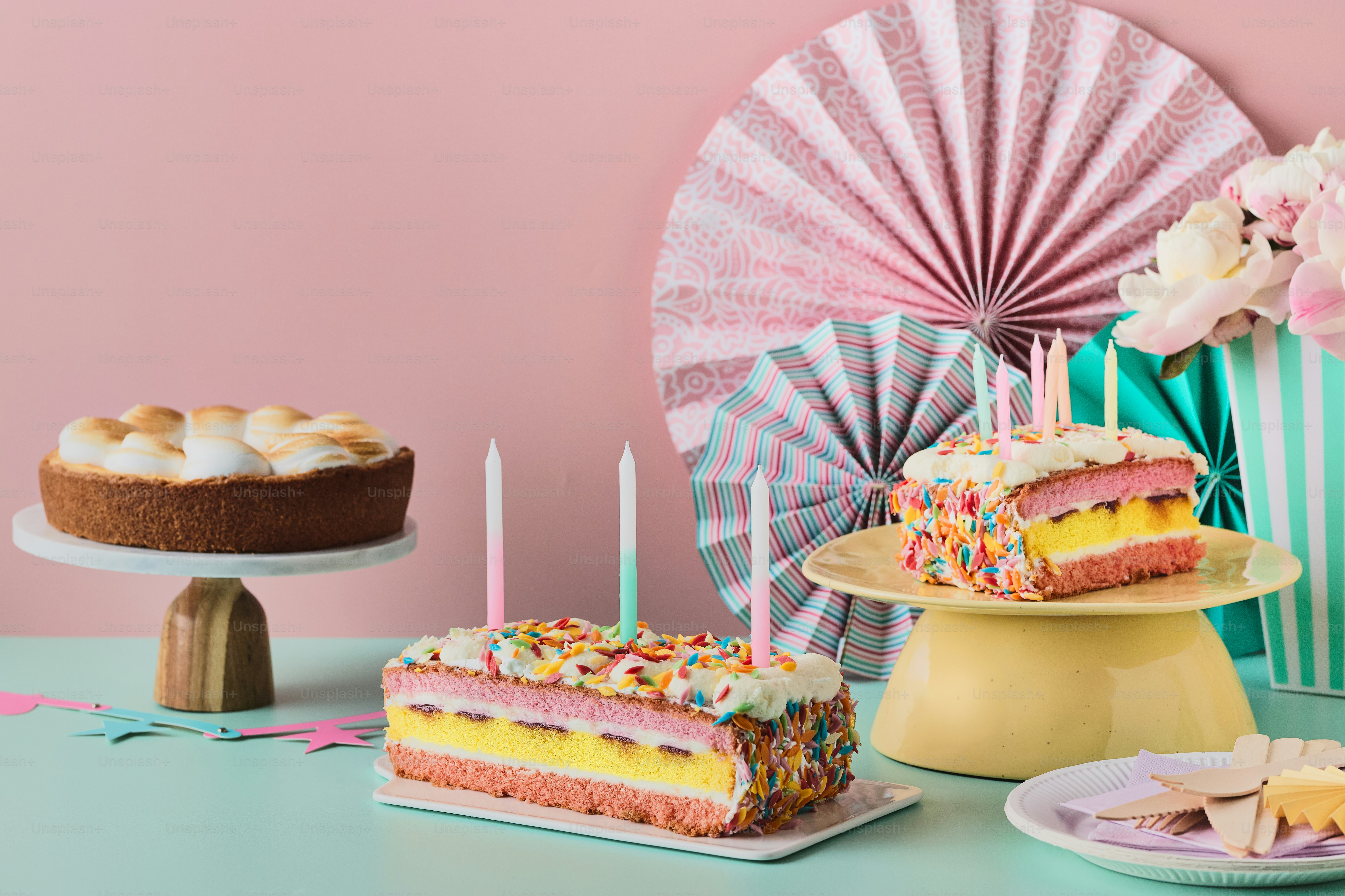 Ein Tisch mit Kuchen und Kerzen neben einer rosa Wand