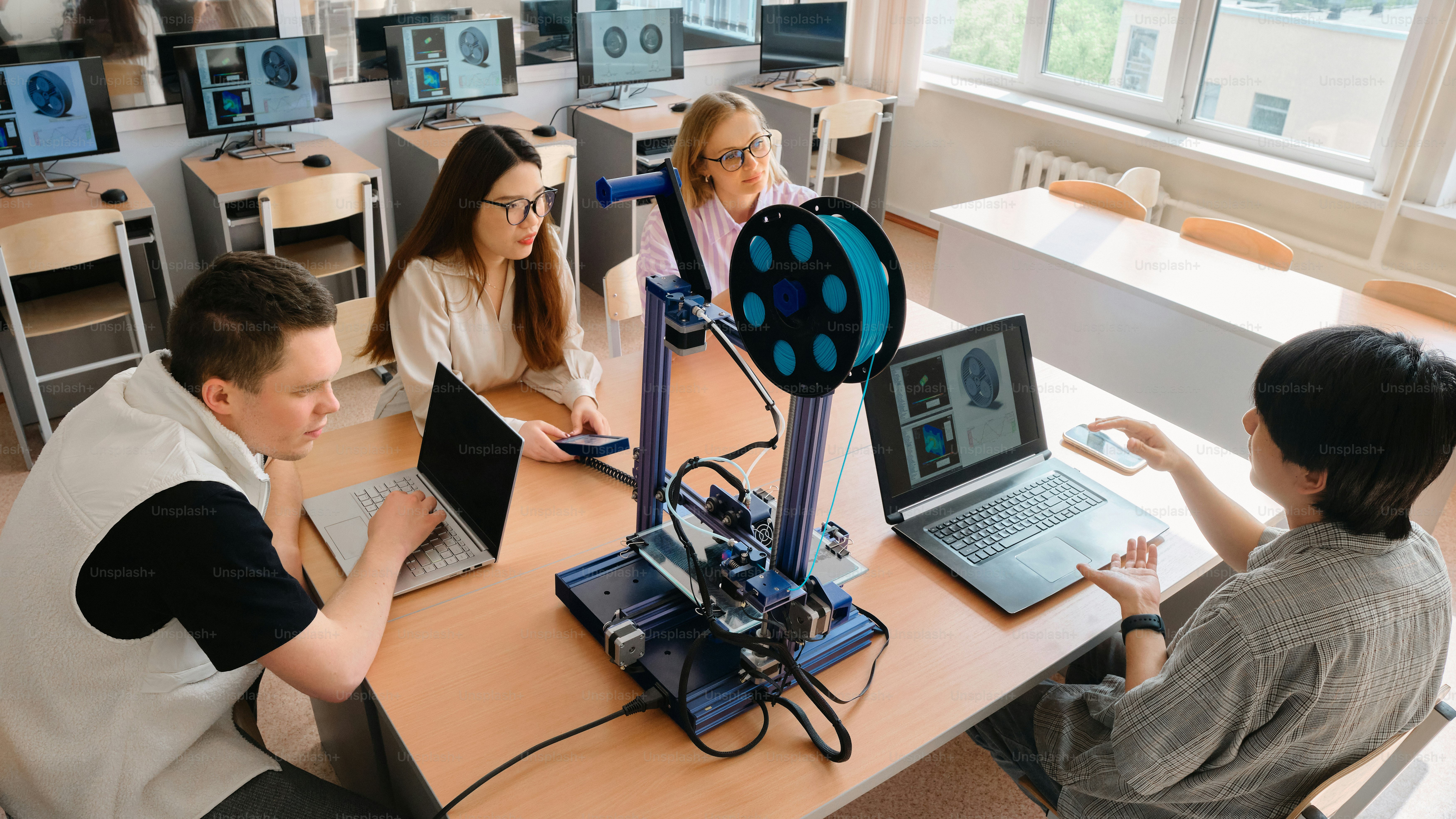 a group of people sitting around a table with laptops