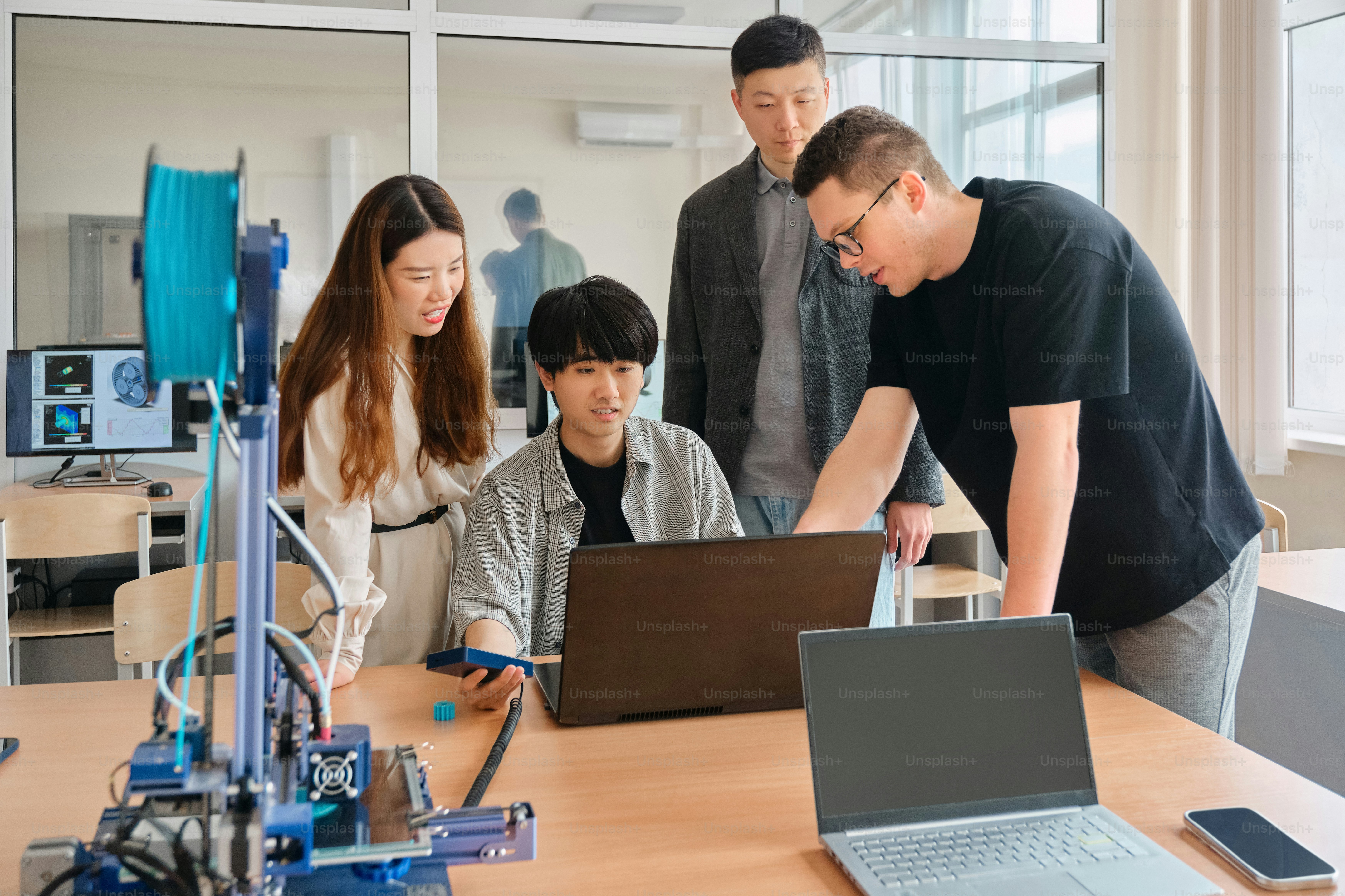 a group of people standing around a table with laptops