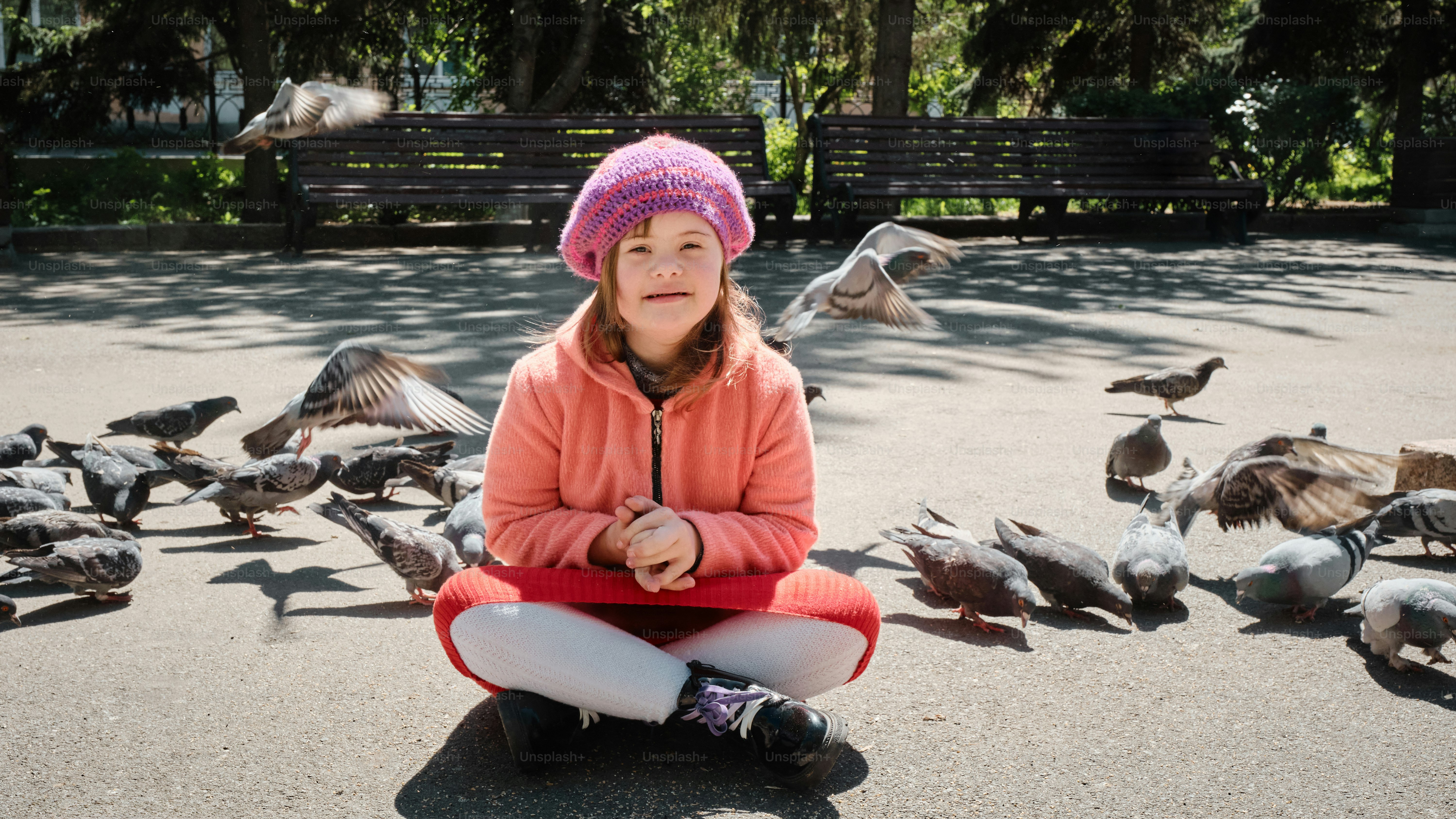 a young girl sitting on the ground surrounded by birds