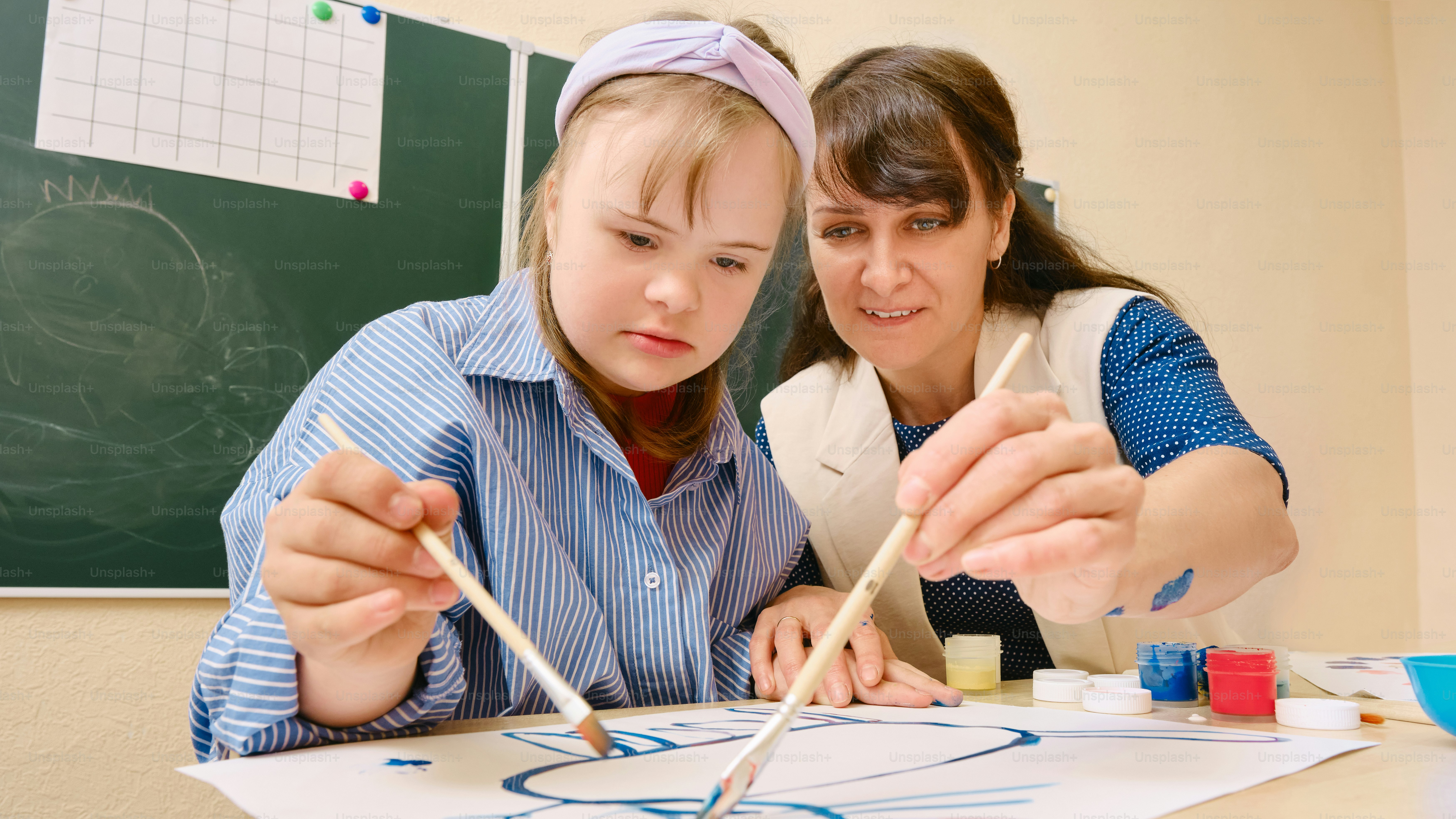 a woman and a girl painting on a piece of paper