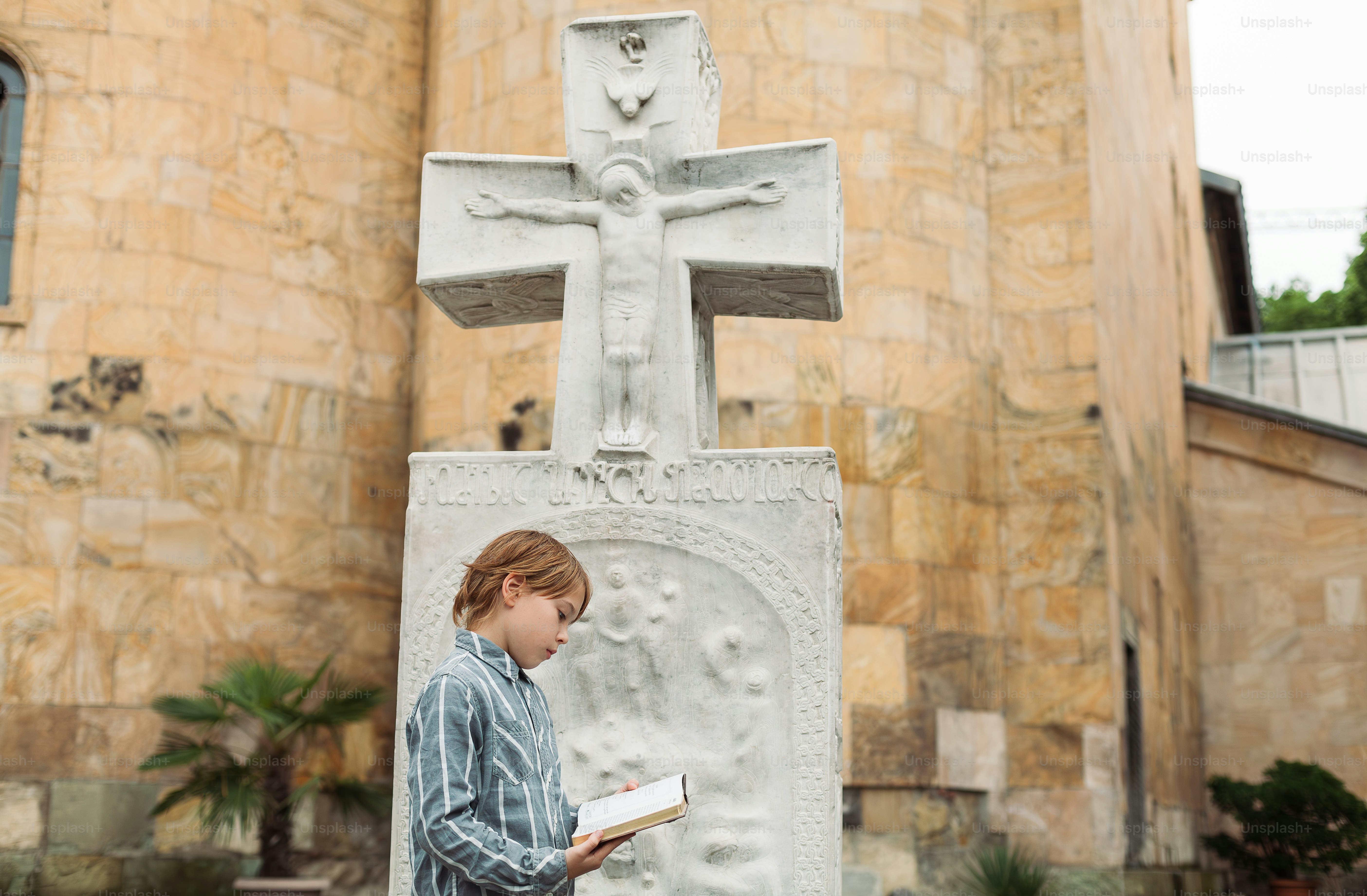 a young girl reading a book in front of a cross