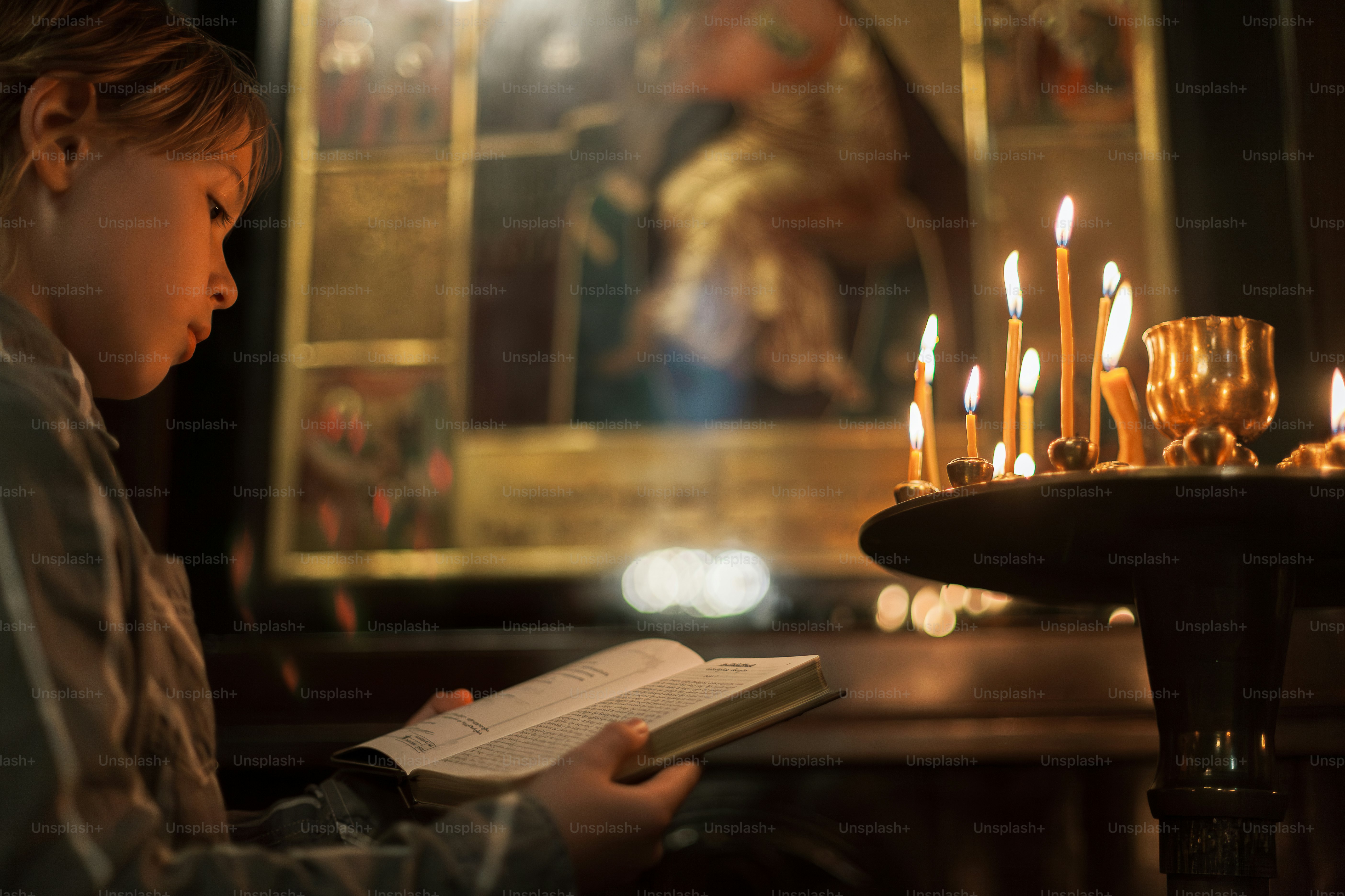 ein kleiner Junge, der vor Kerzen ein Buch liest