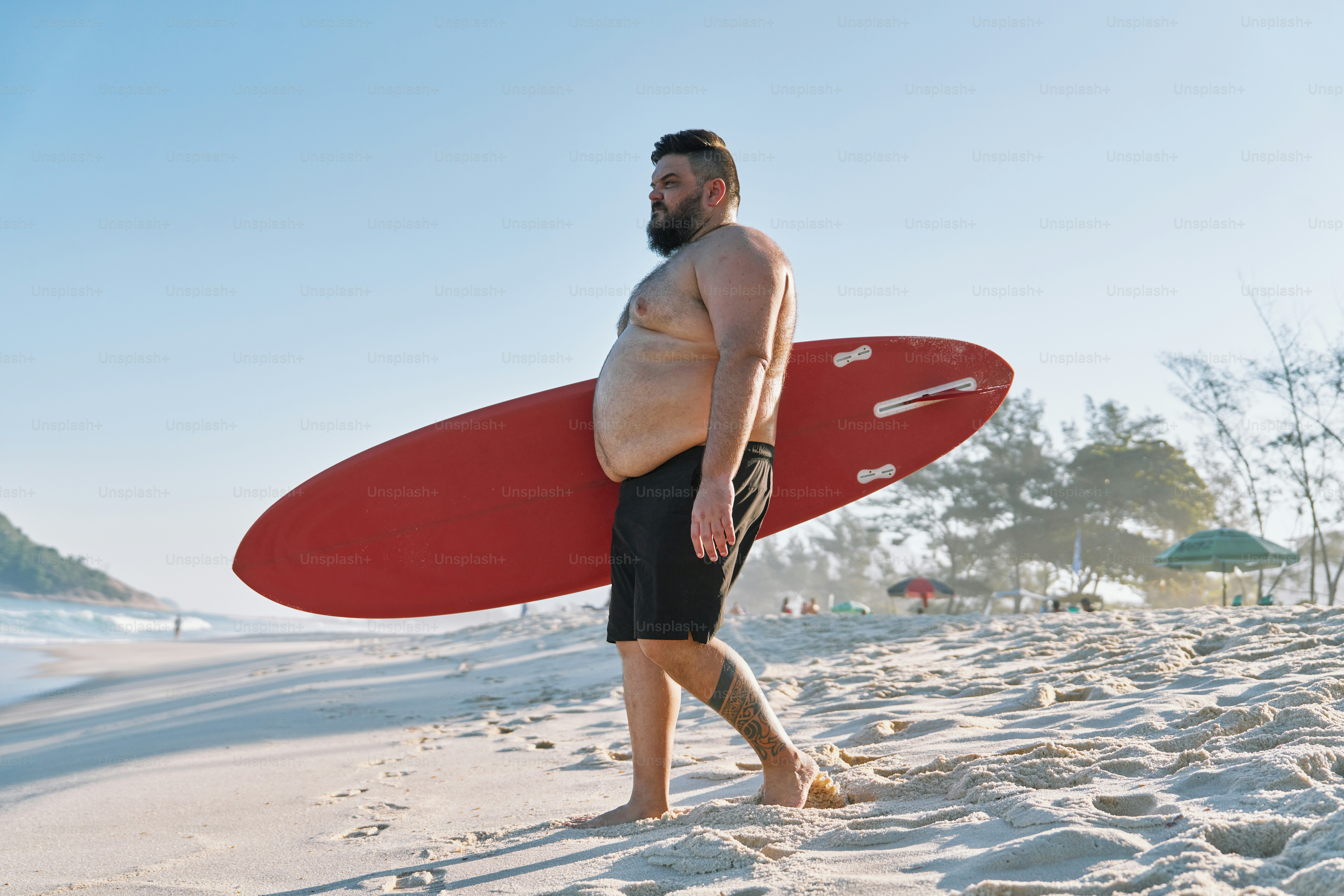 a man standing on a beach holding a red surfboard