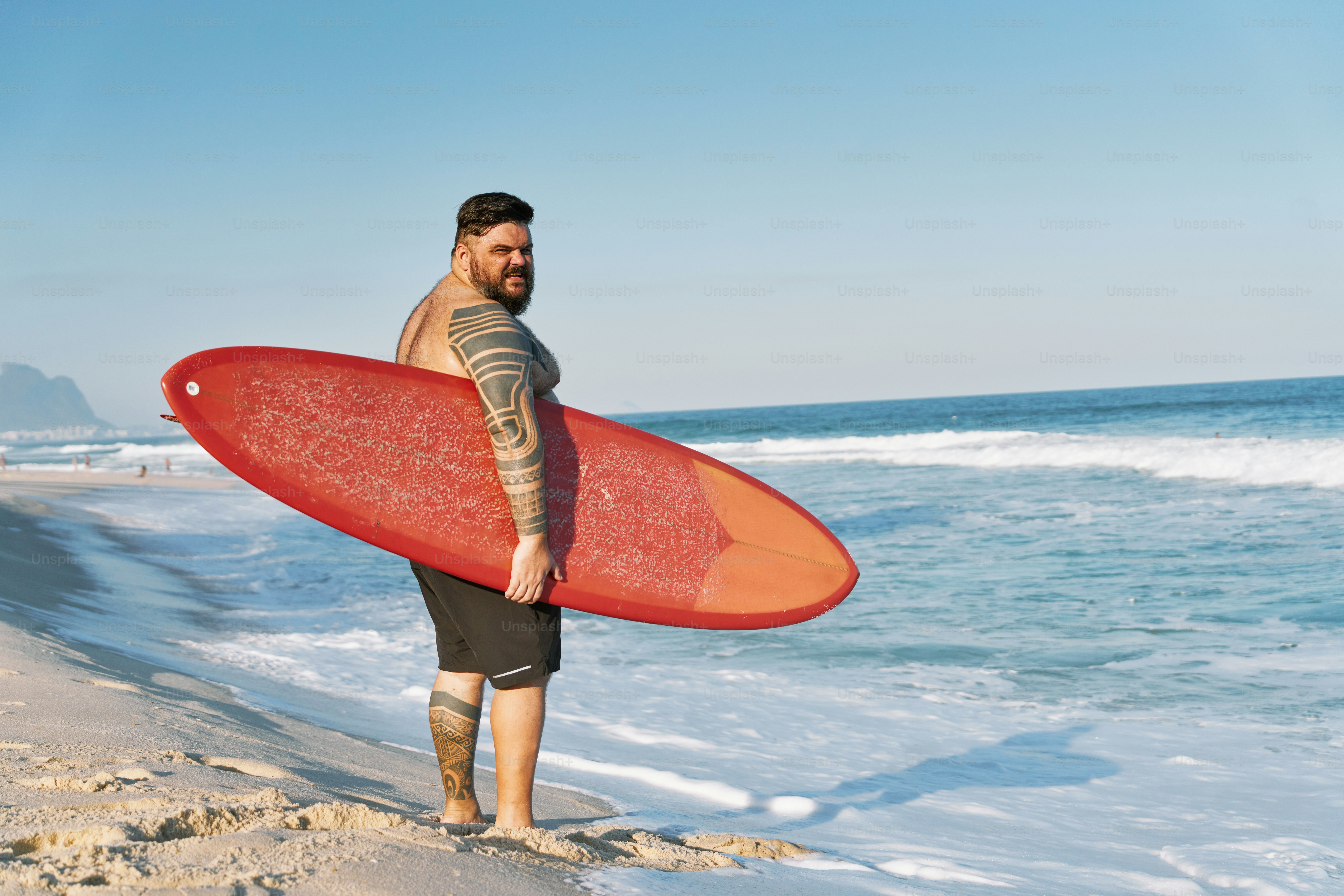 a man standing on a beach holding a red surfboard