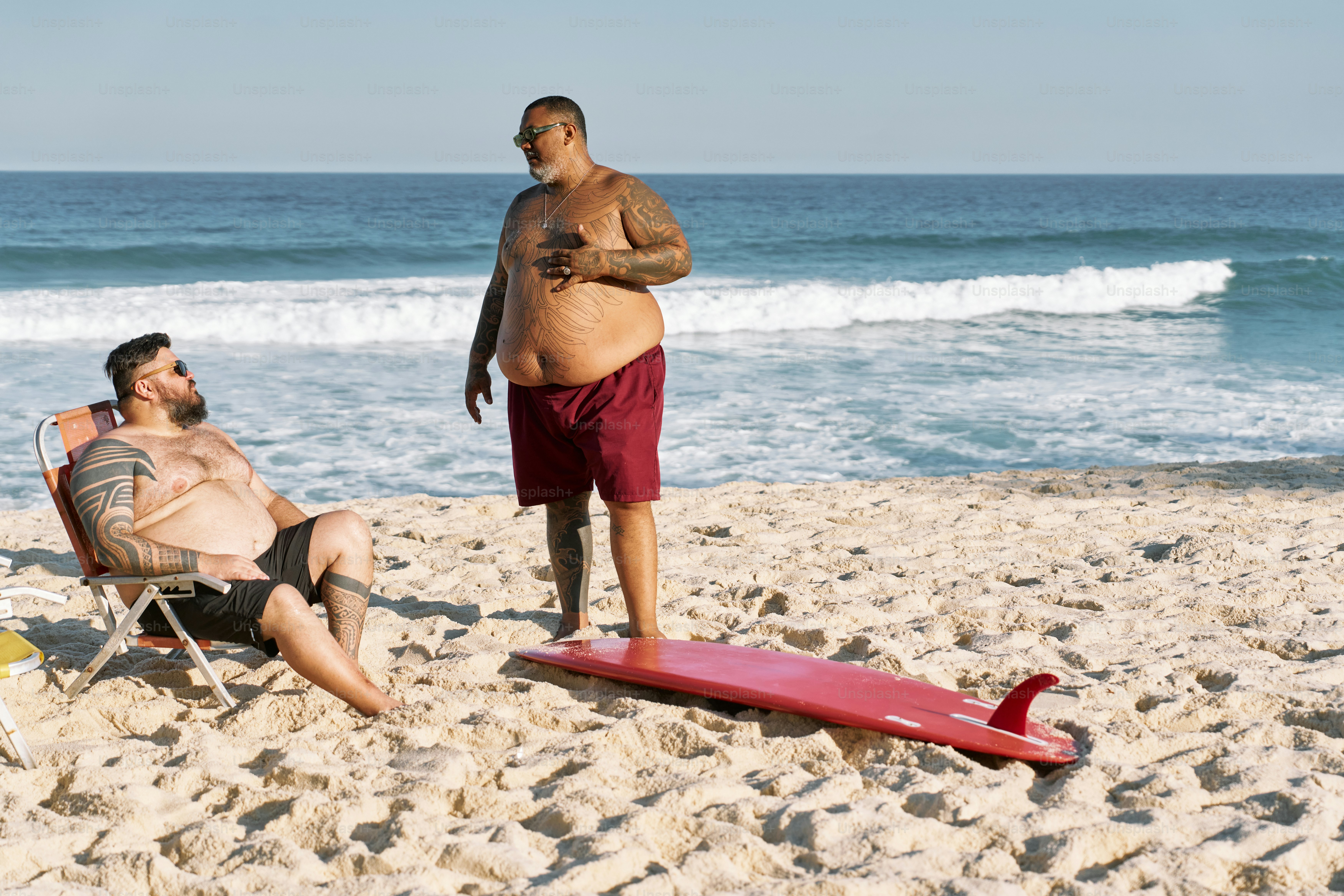 a man standing next to a red surfboard on a beach
