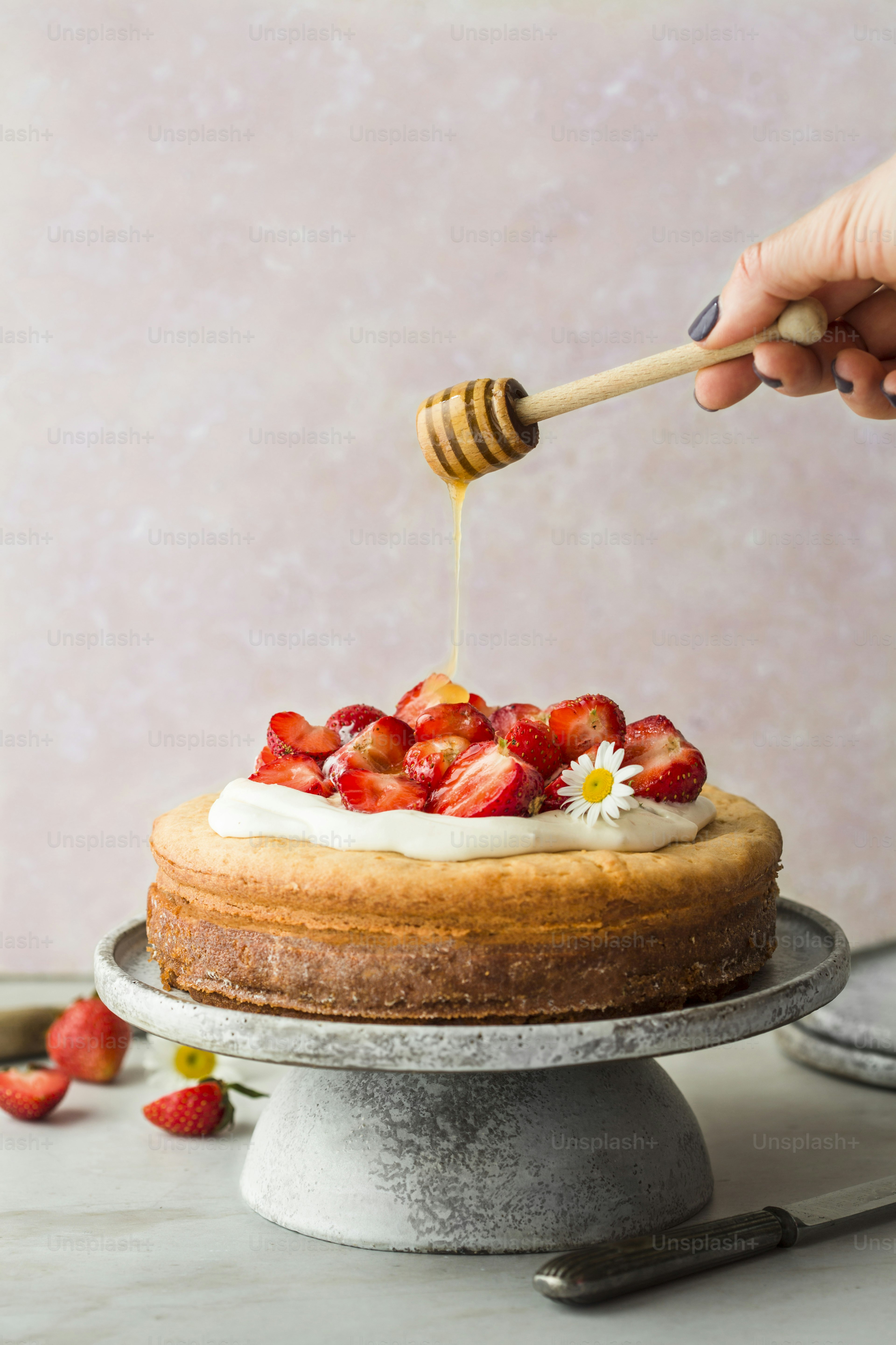 a person drizzling honey onto a cake with strawberries