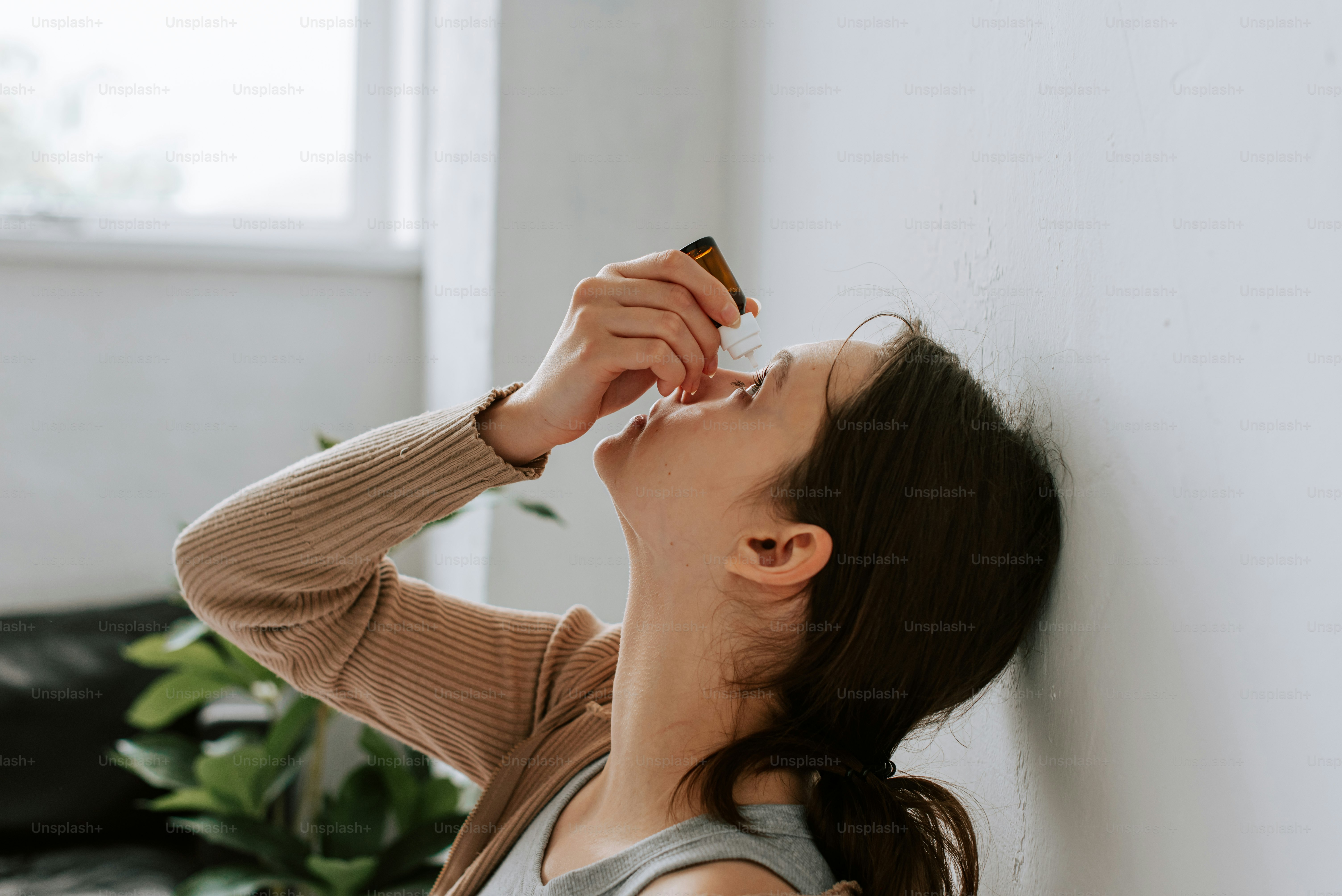 a woman is leaning against a wall and drinking from a bottle