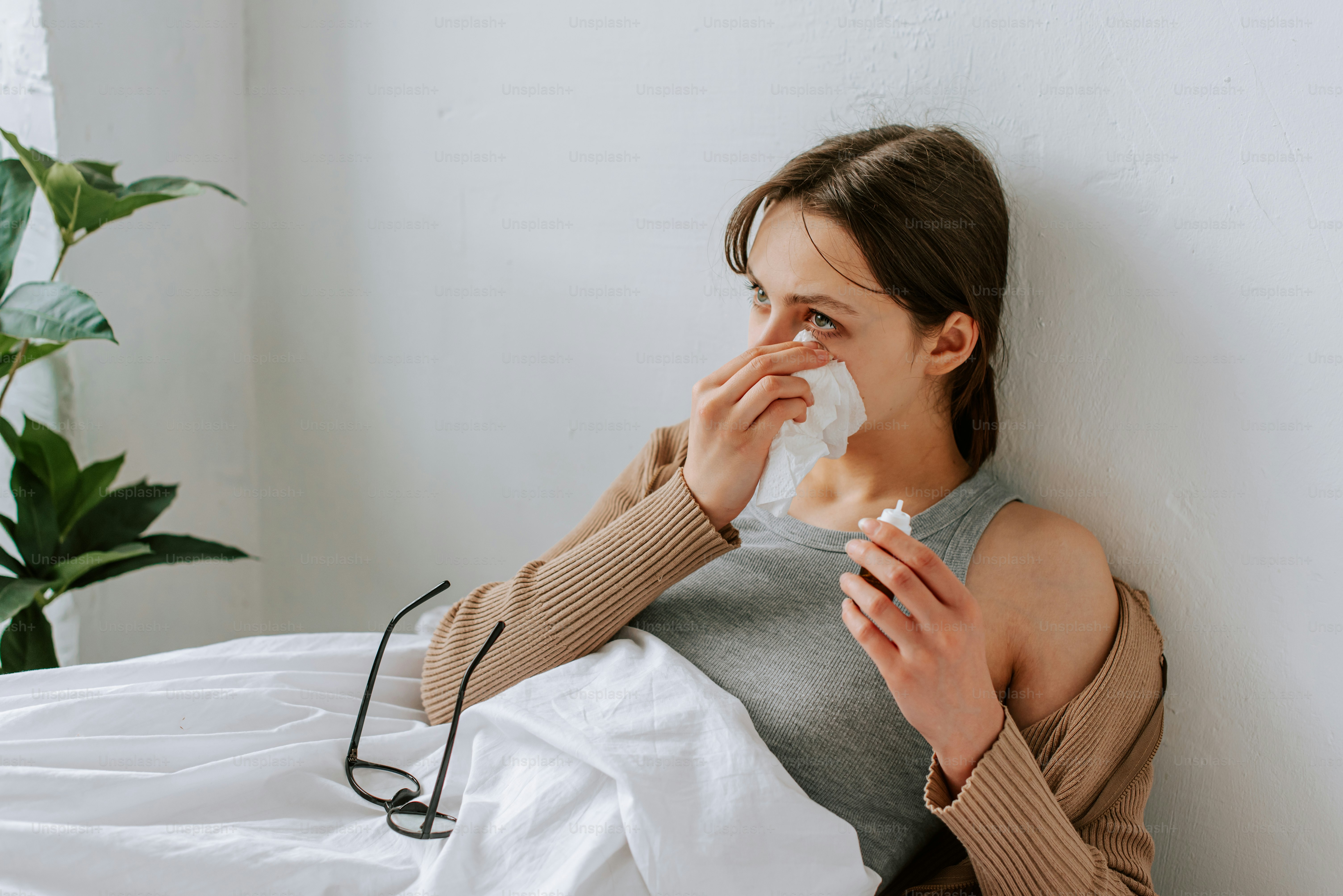 a woman sitting on a bed blowing her nose