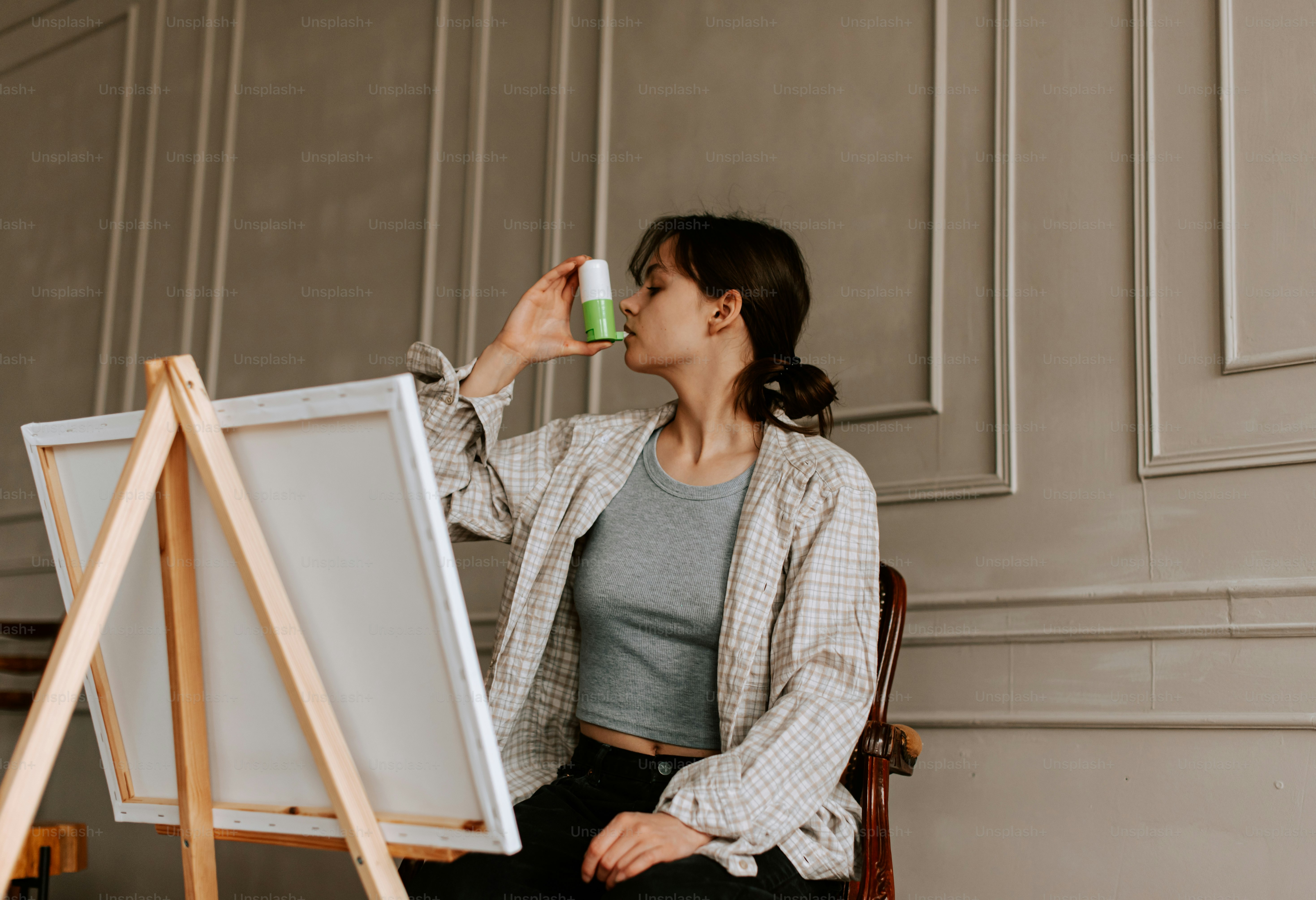 a woman sitting in front of a easel drinking from a cup