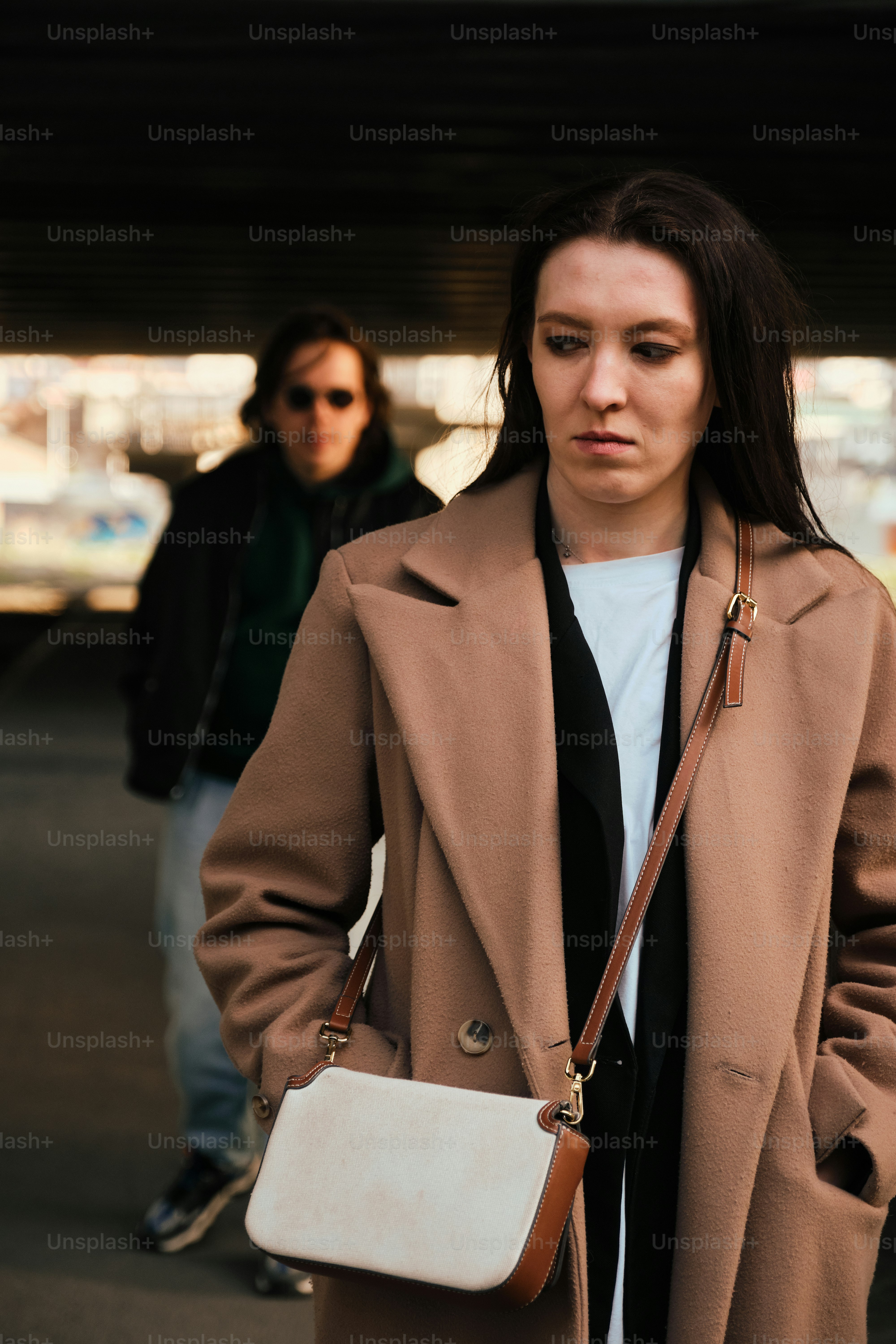 a woman in a brown coat carrying a white purse