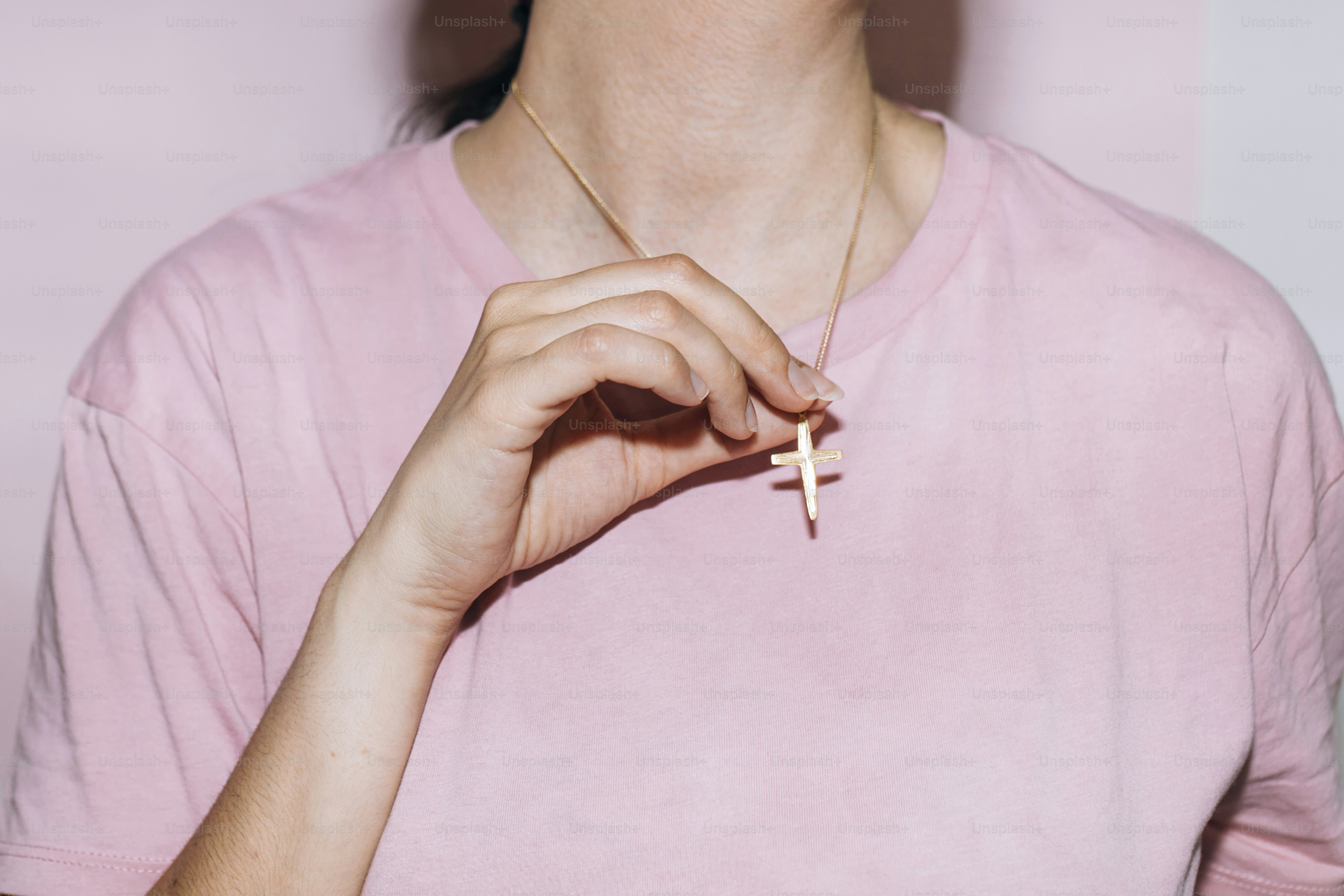 a woman wearing a pink shirt holding a cross necklace