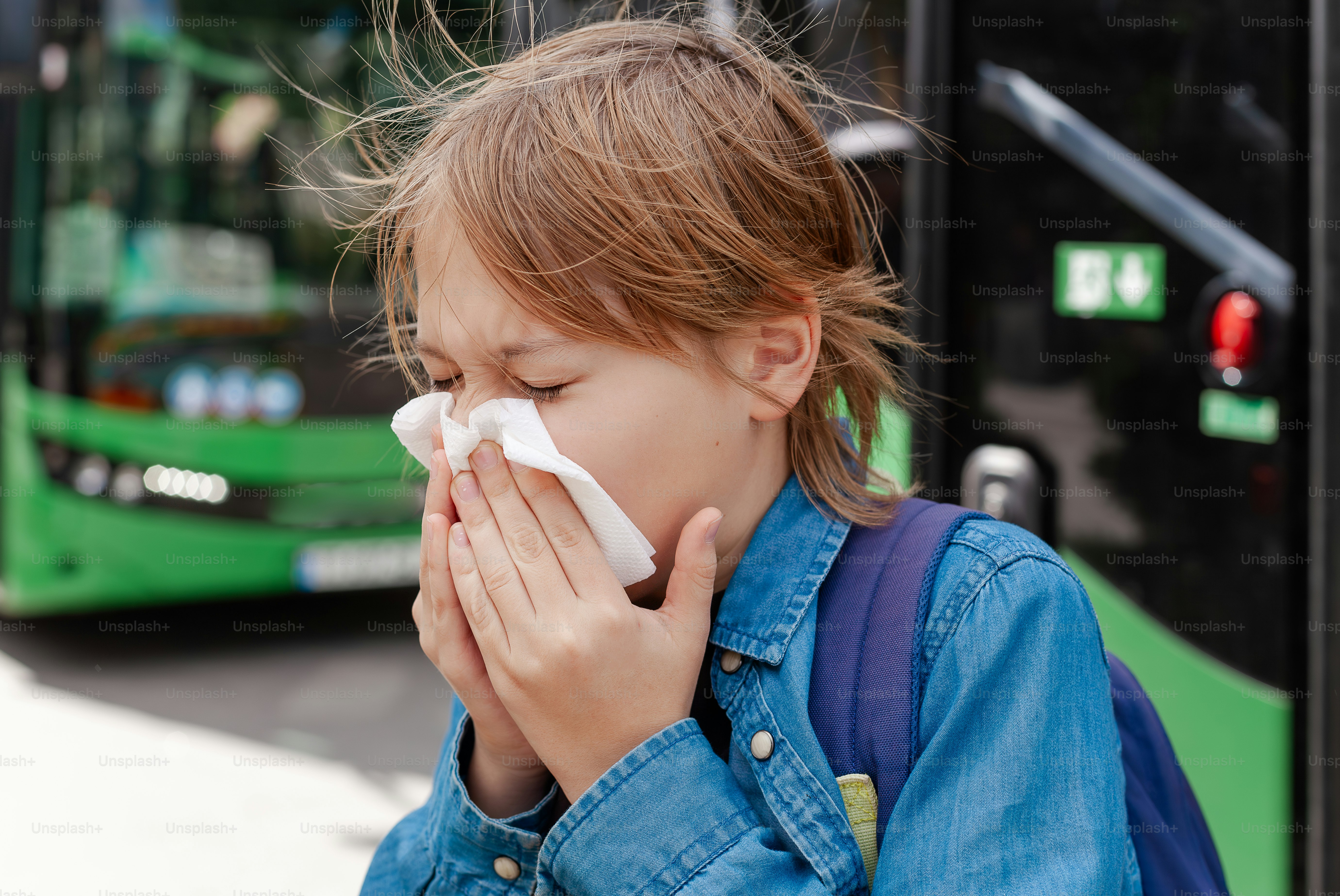 a little girl blowing her nose next to a green bus