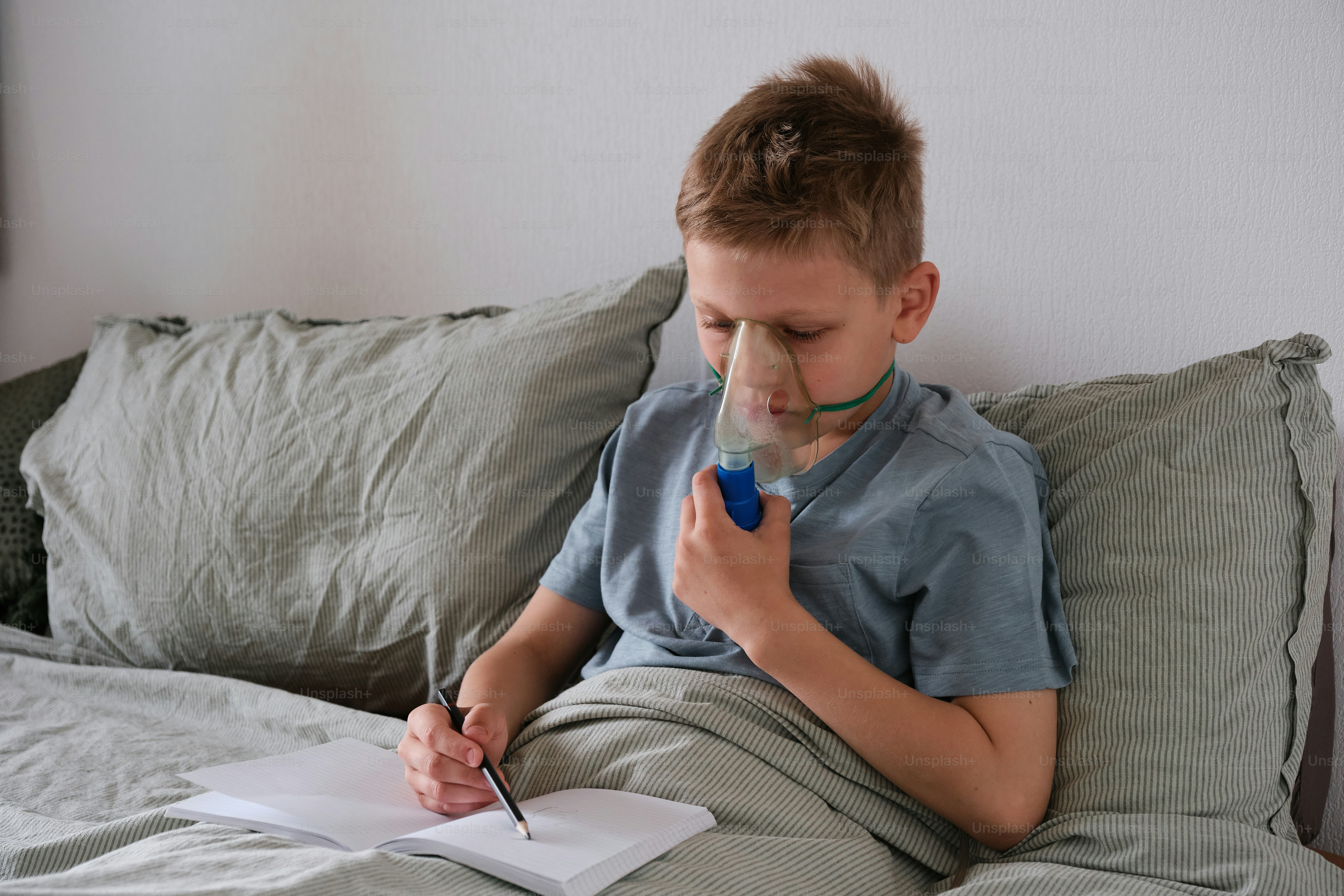 a young boy sitting on a bed writing on a piece of paper