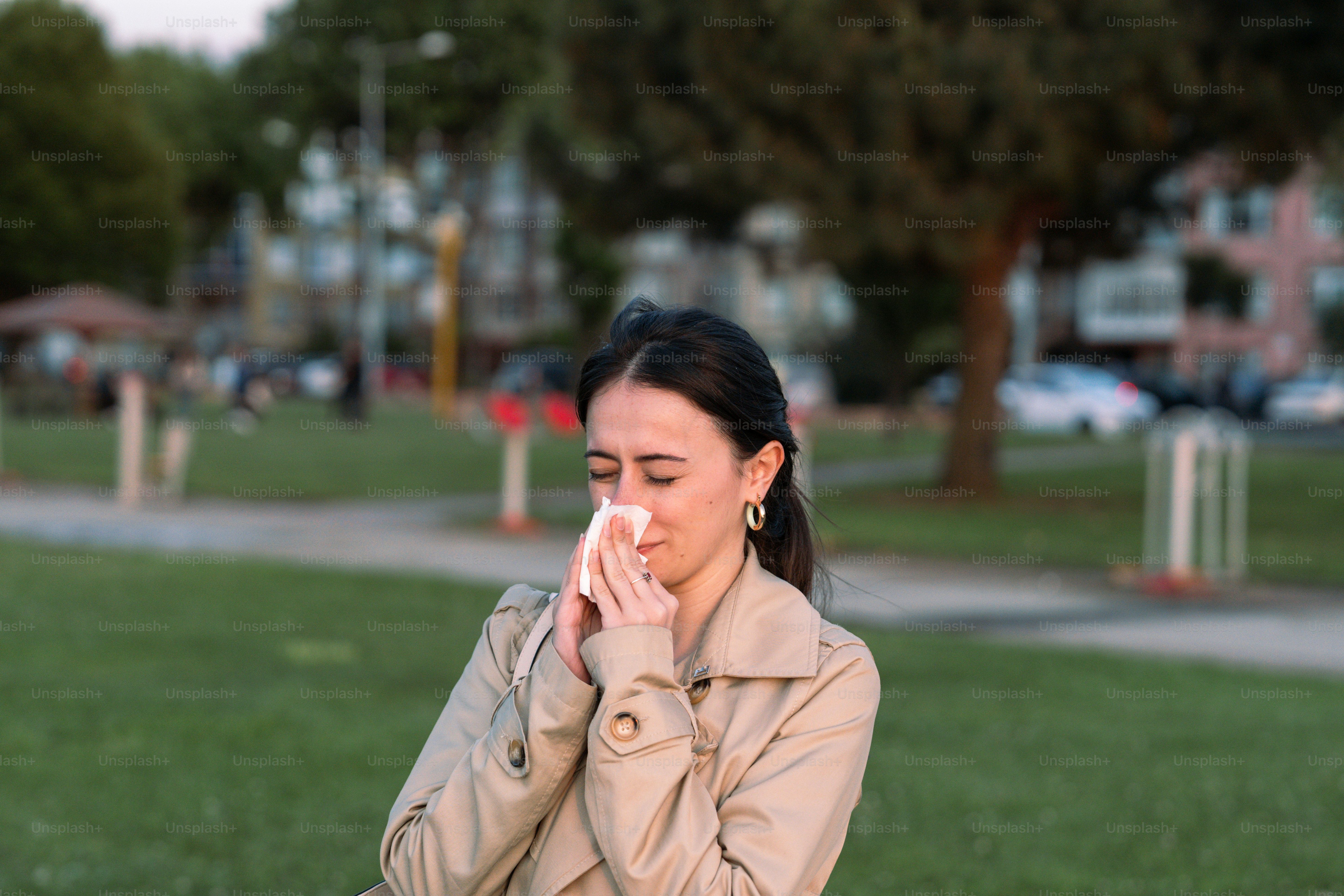 a woman sitting on a park bench blowing her nose
