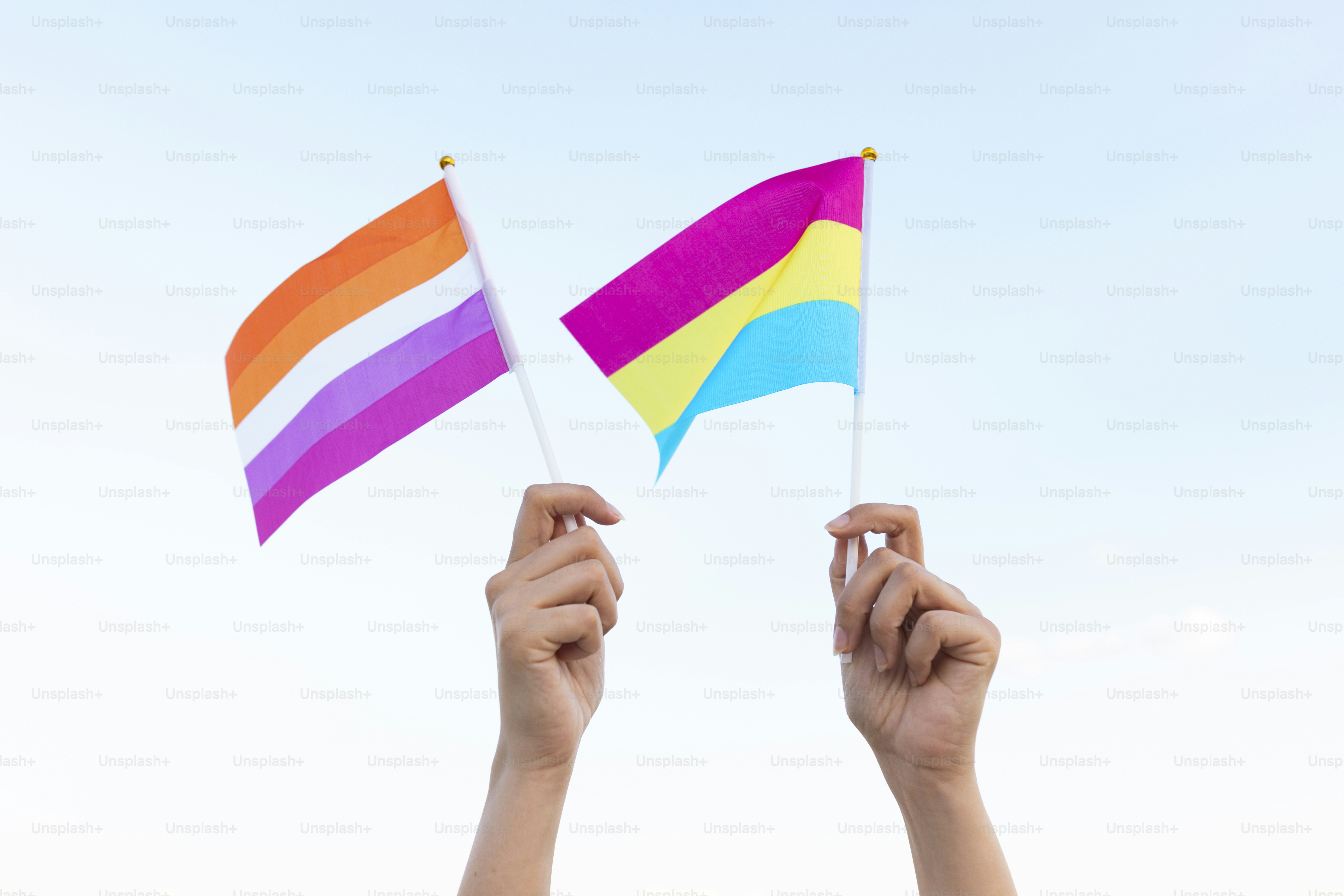 Dos manos sosteniendo una bandera del arco iris contra un cielo azul