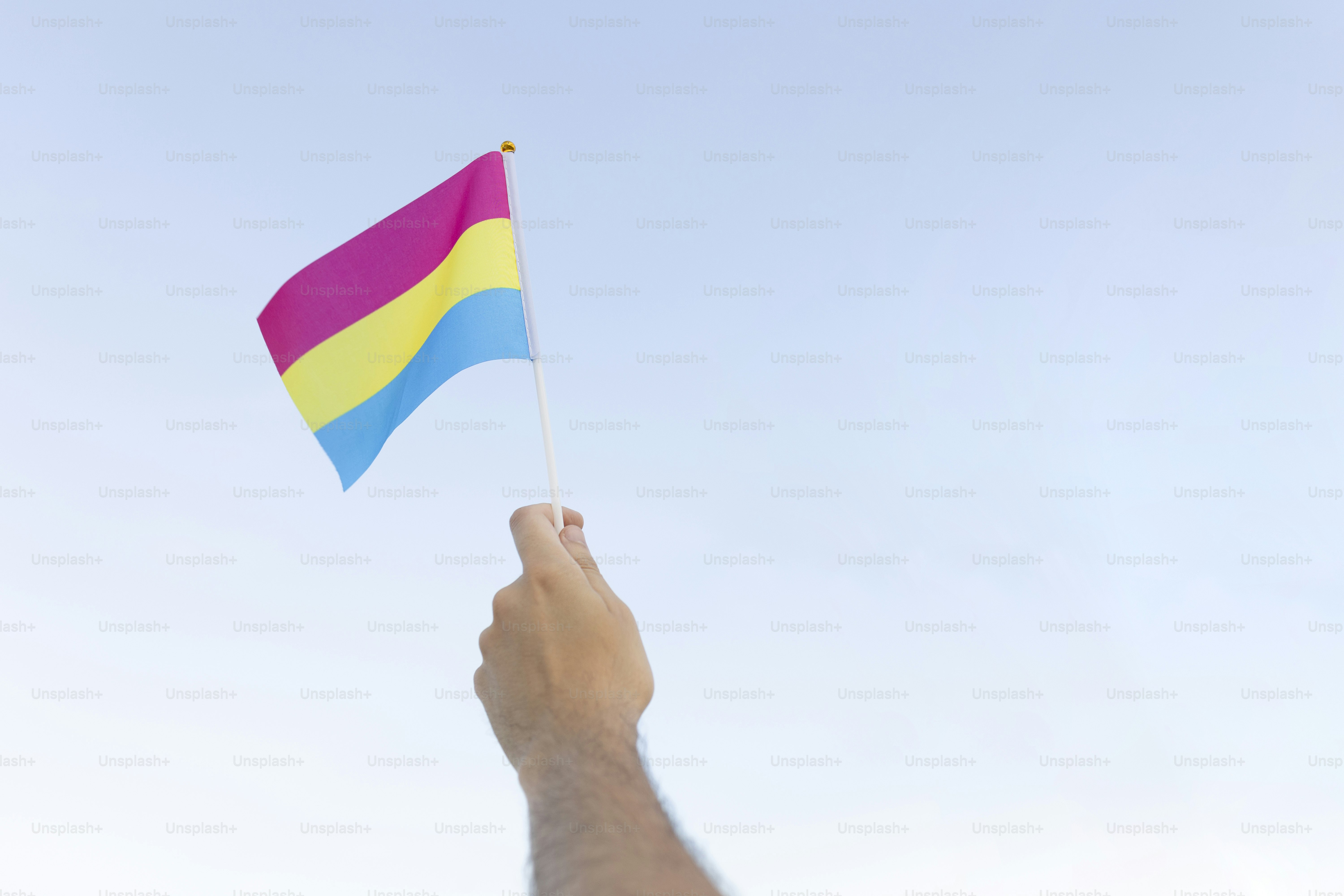 una mano sosteniendo una bandera con los colores del arco iris contra un cielo azul