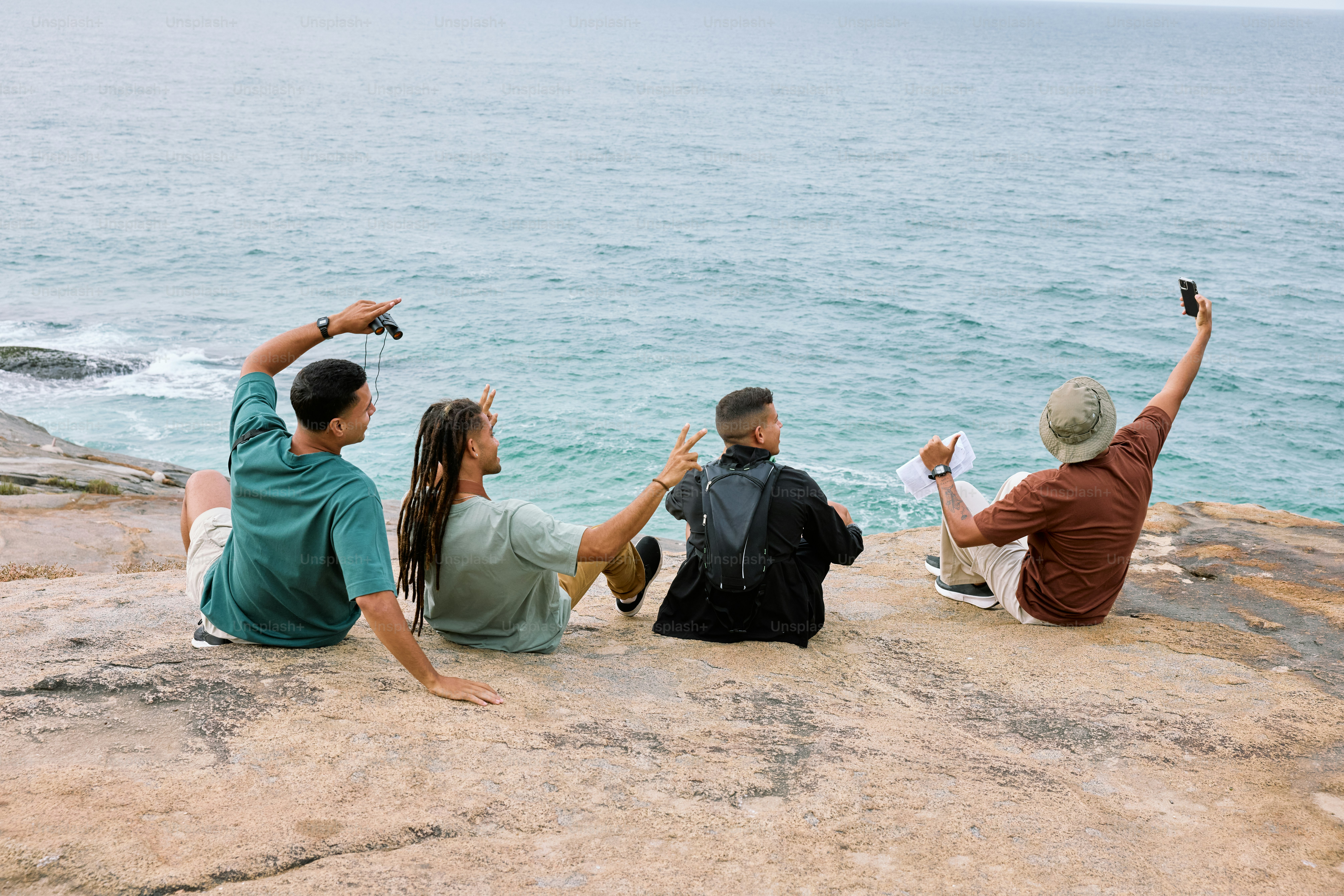 a group of people sitting on top of a rock next to the ocean