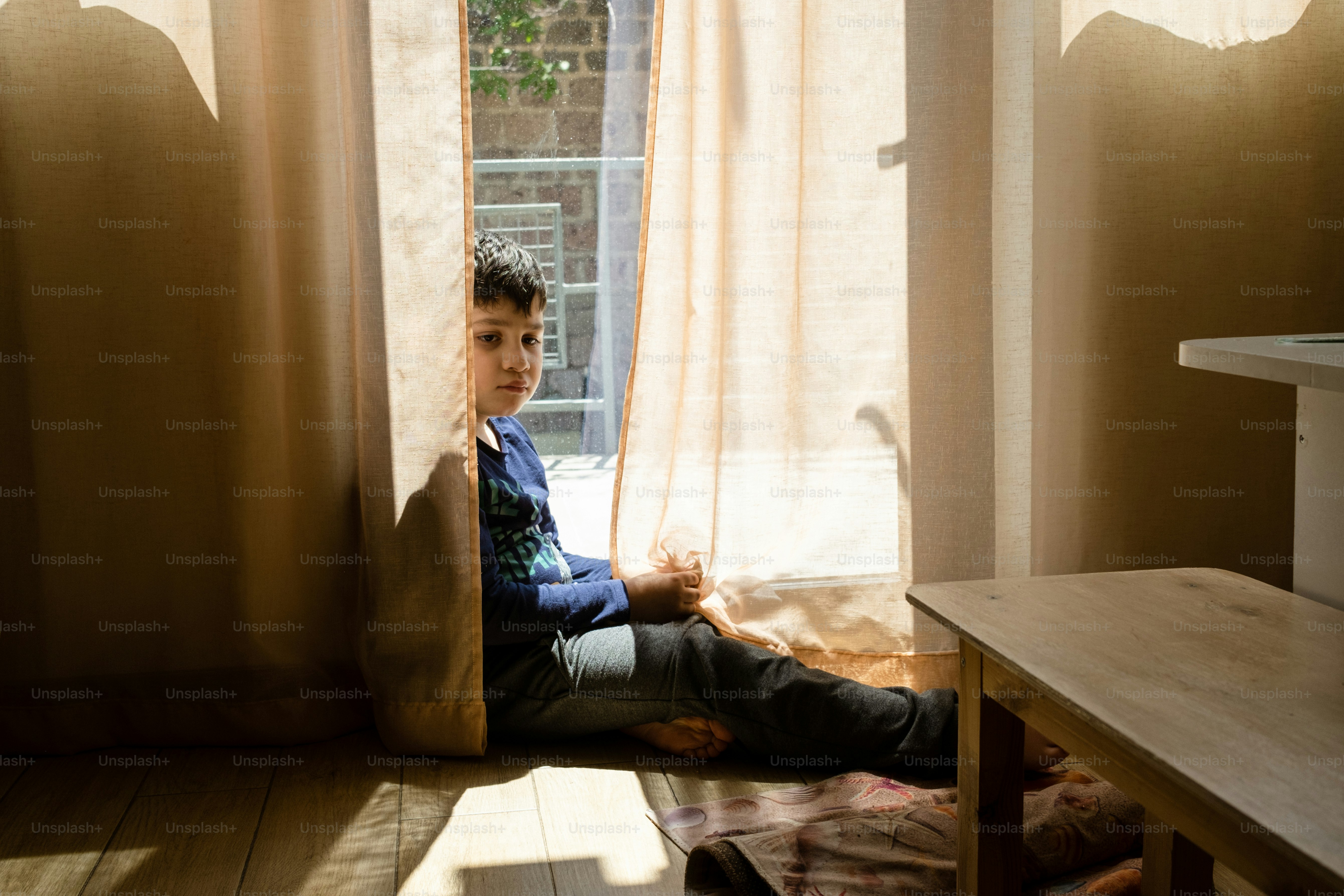 a young boy sitting on the floor in front of a window