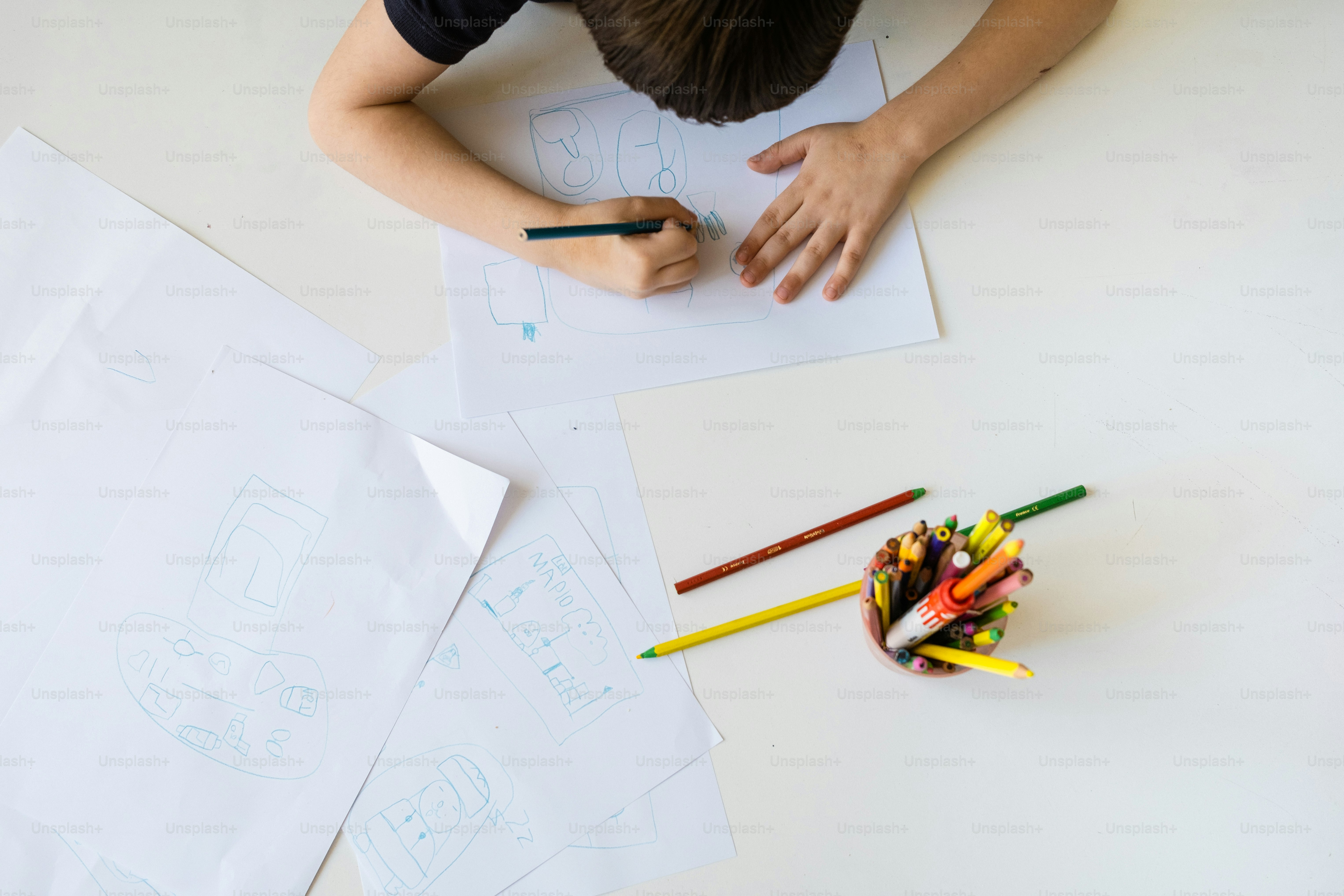a young boy sitting at a table with crayons and pencils