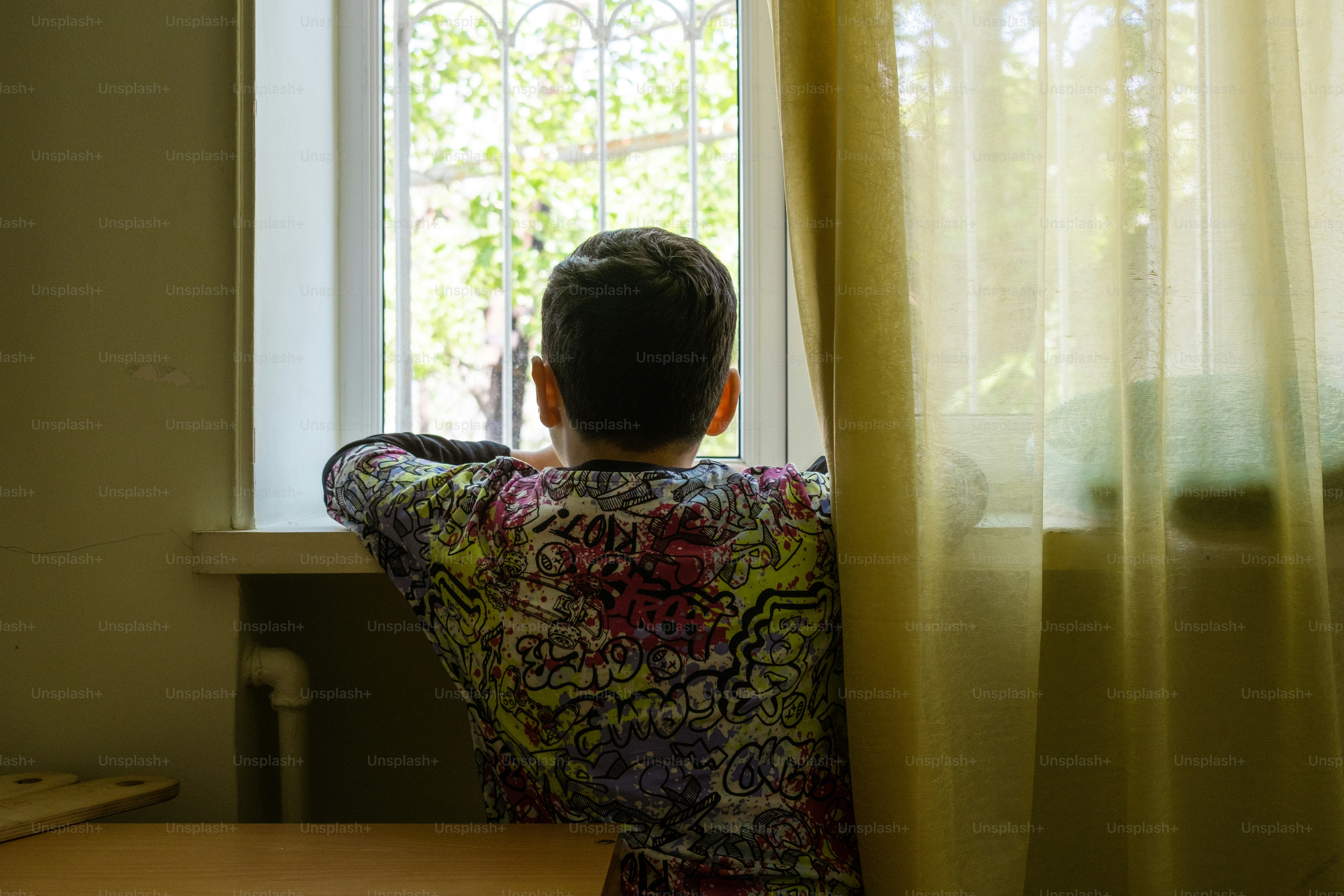 a boy looking out of a window with a green curtain
