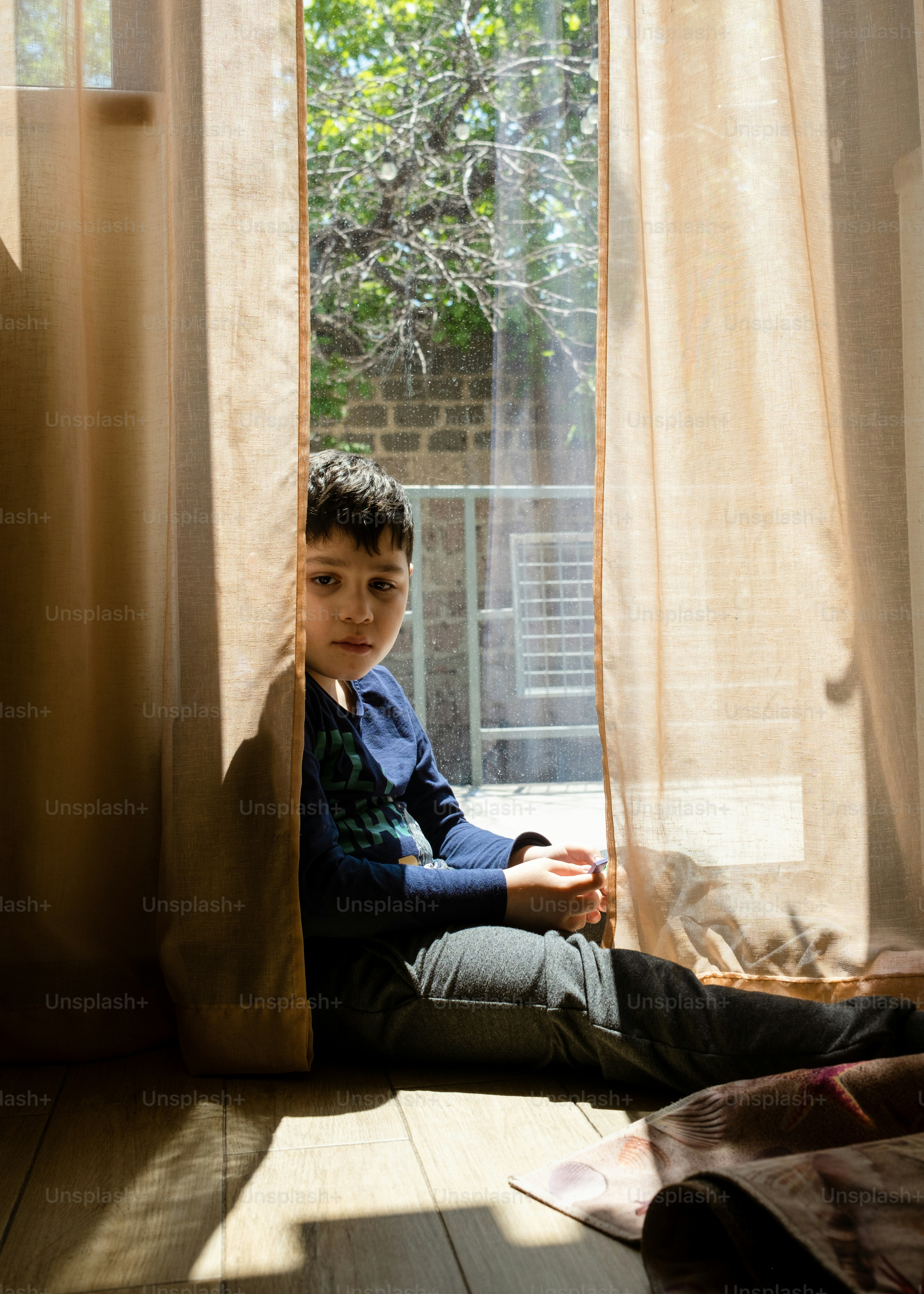 a young boy sitting on the floor in front of a window