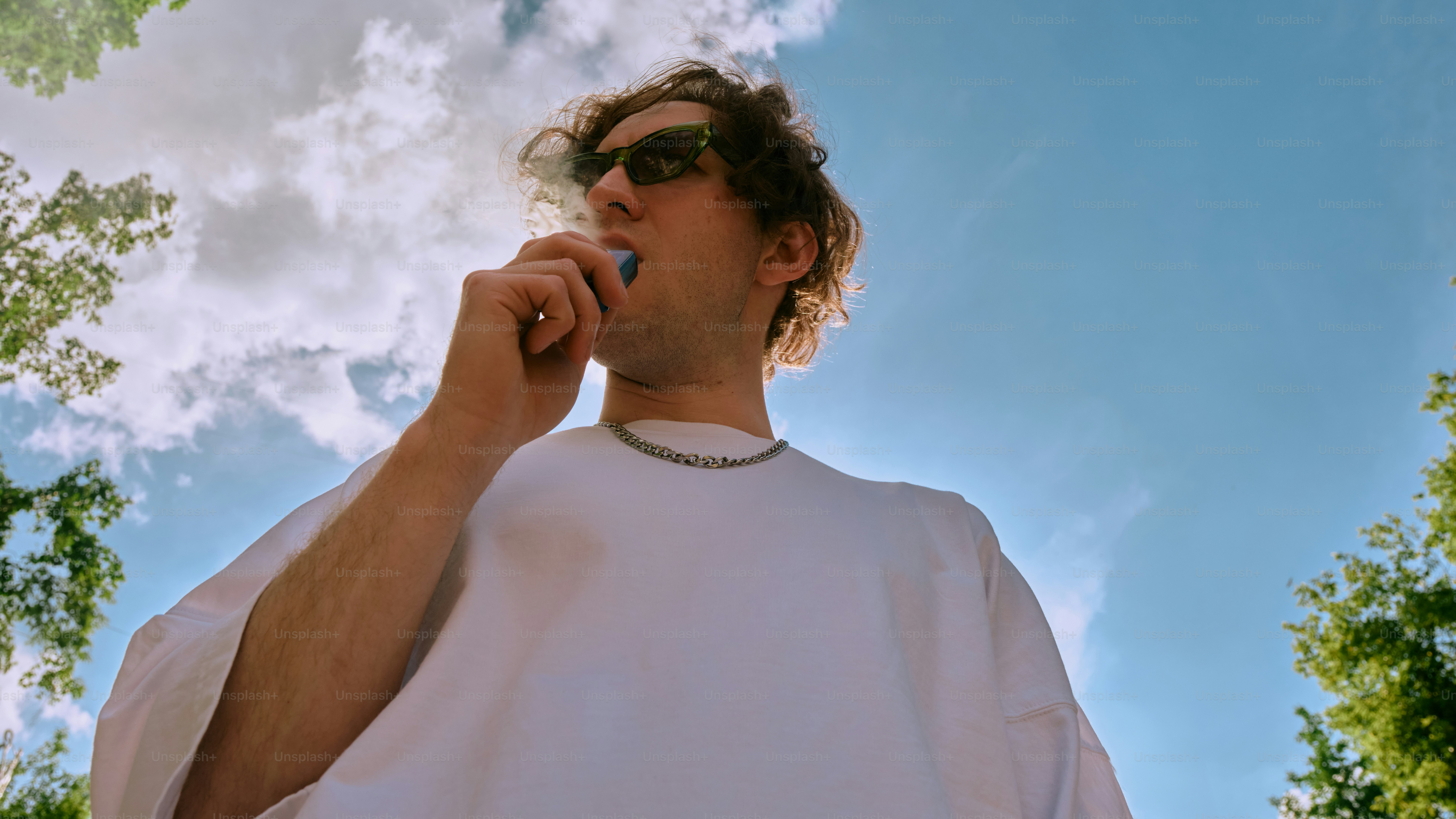 a man wearing sunglasses and a white shirt is talking on a cell phone