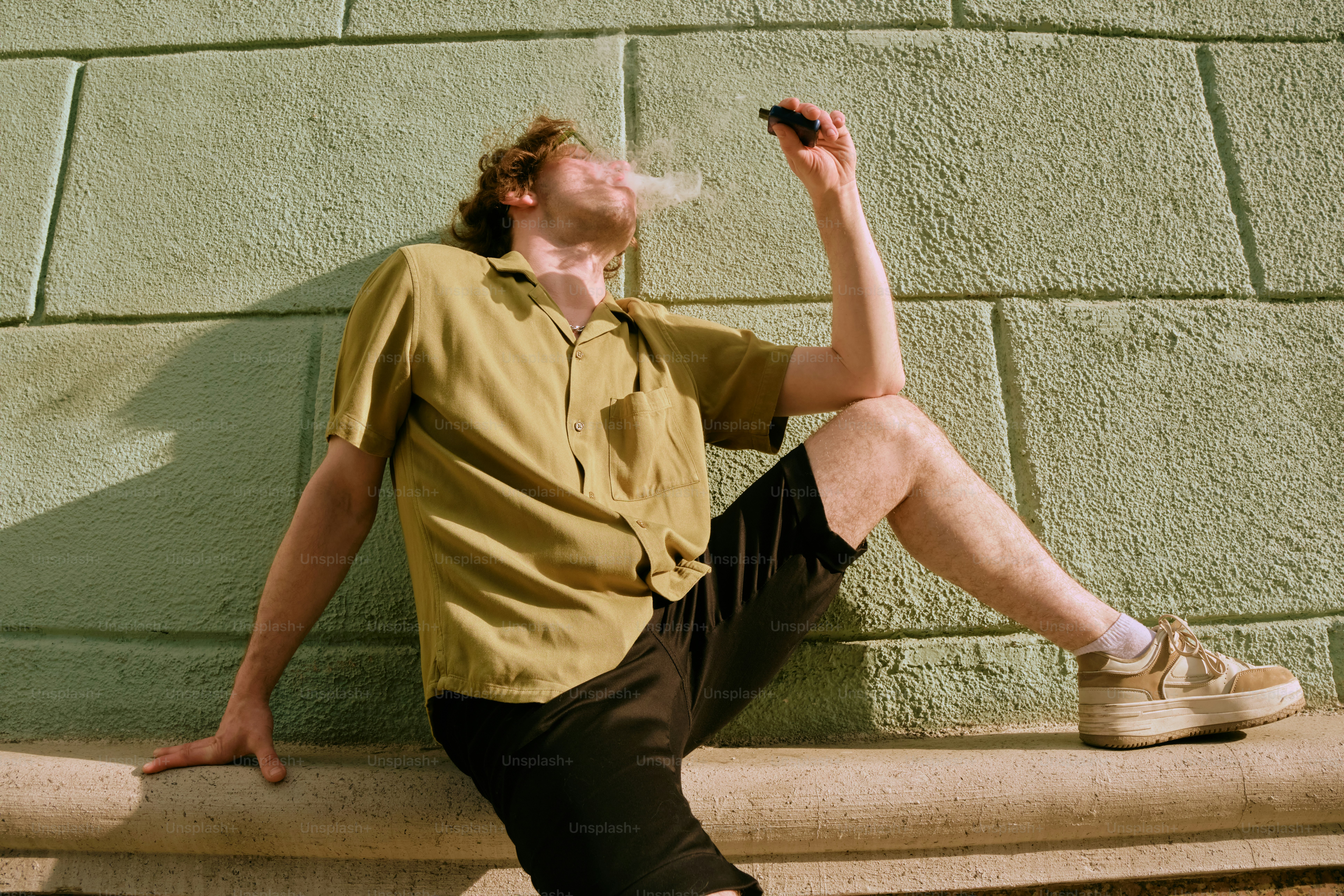 a man sitting on a ledge smoking a cigarette