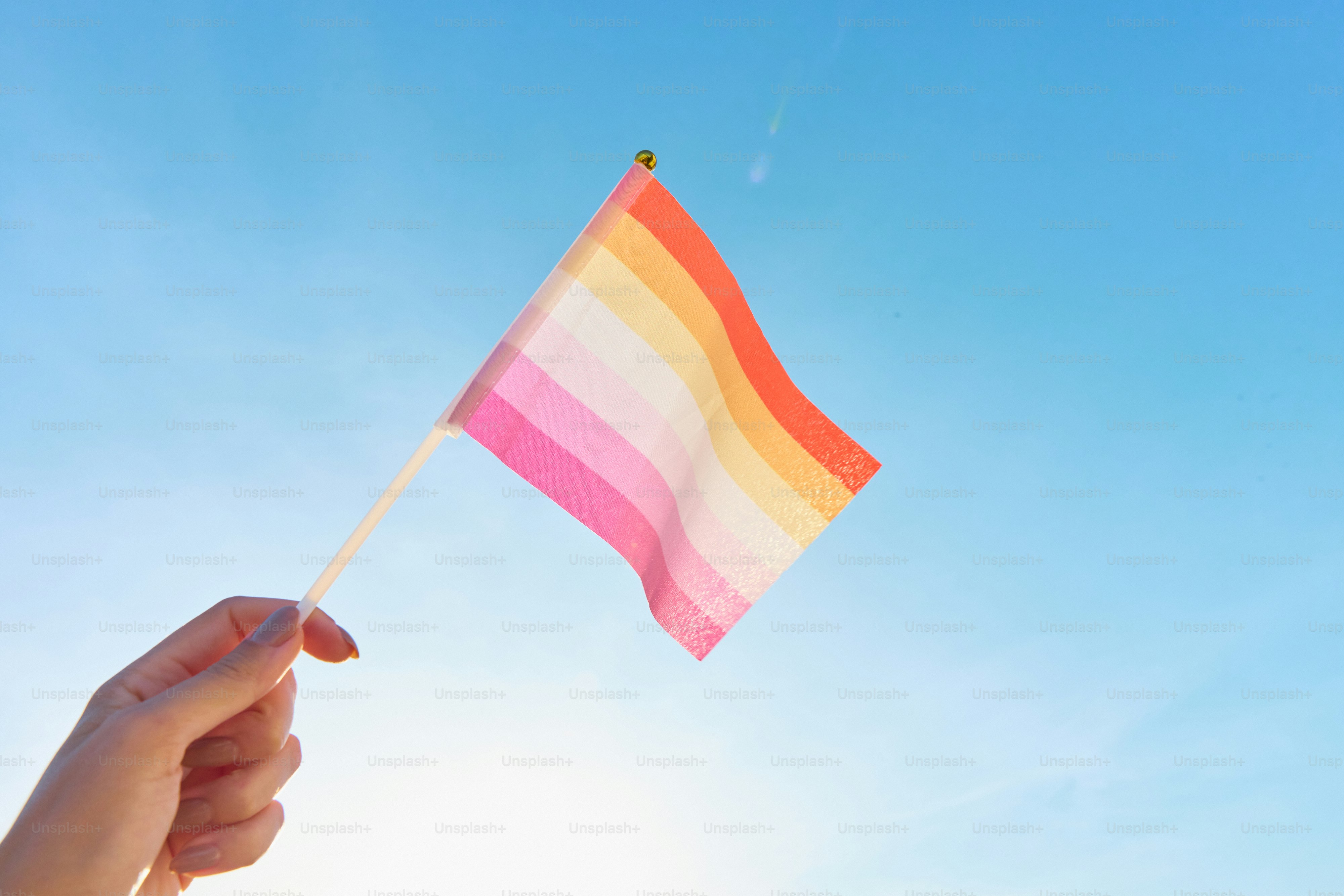 Uma mão segurando uma bandeira do arco-íris ao sol