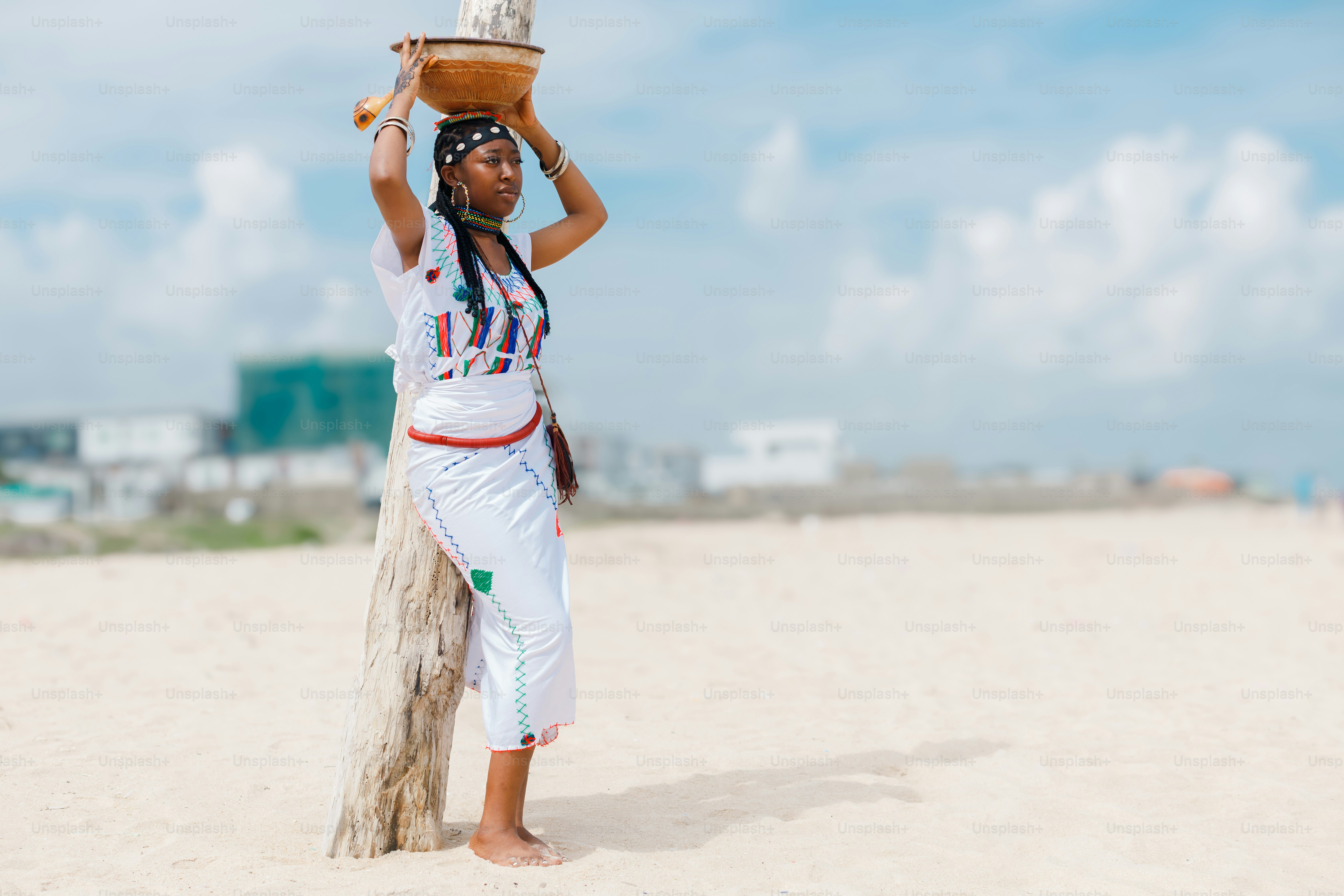 A woman standing on a beach holding a basket on her head