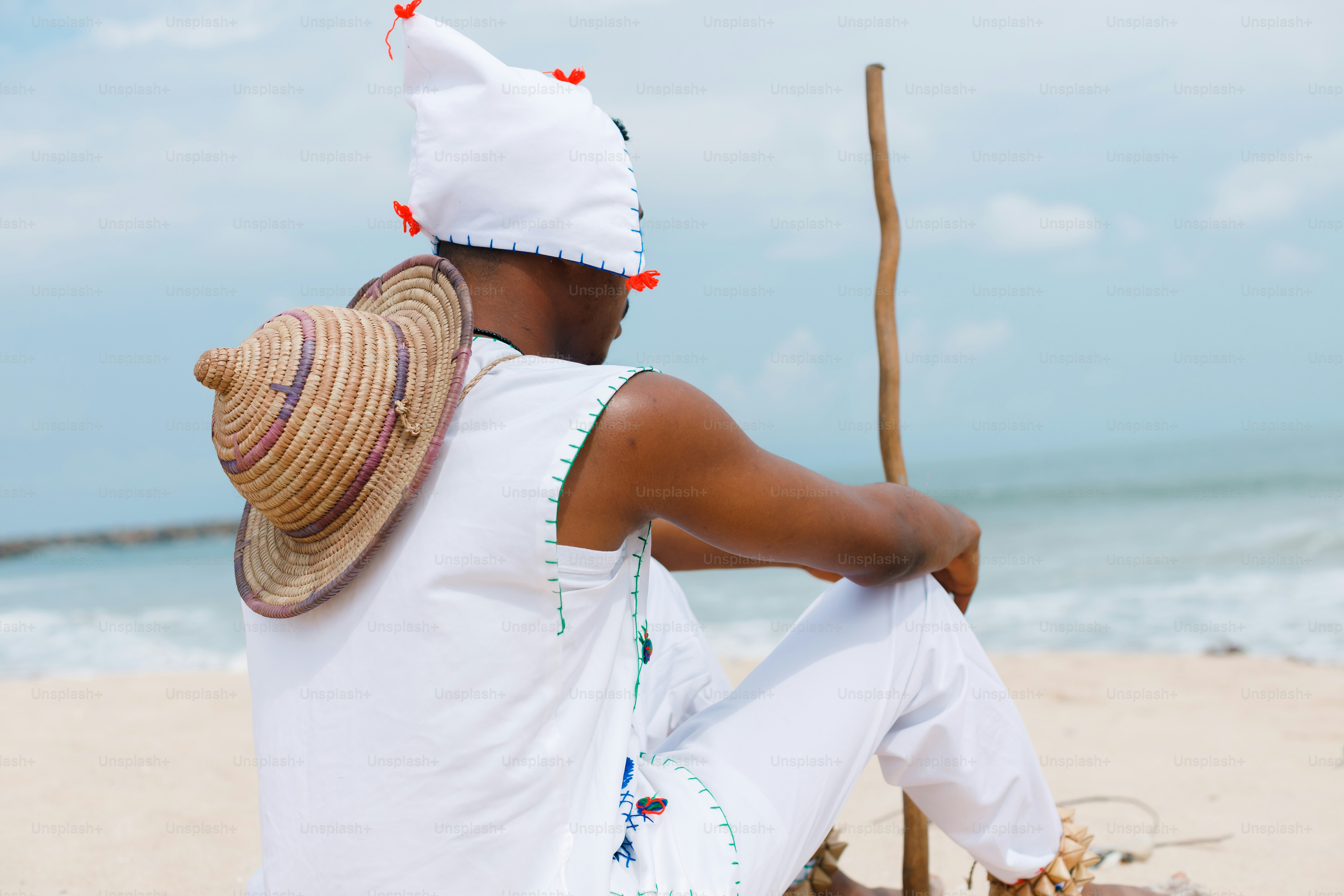 A man sitting on a beach with a hat on